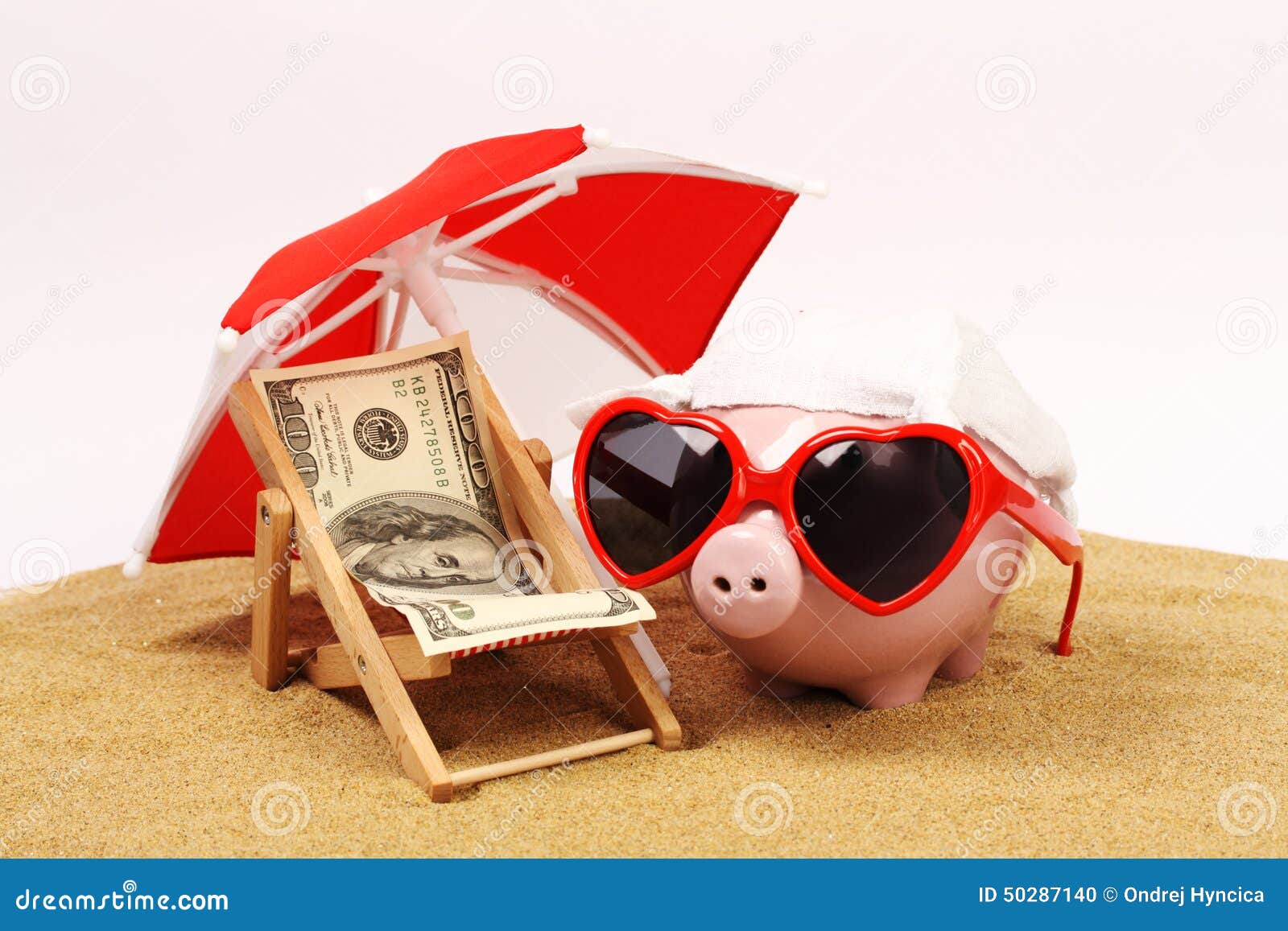 summer piggy bank with heart sunglasses standing on sand under red and white sunshade next to beach chair with towel from