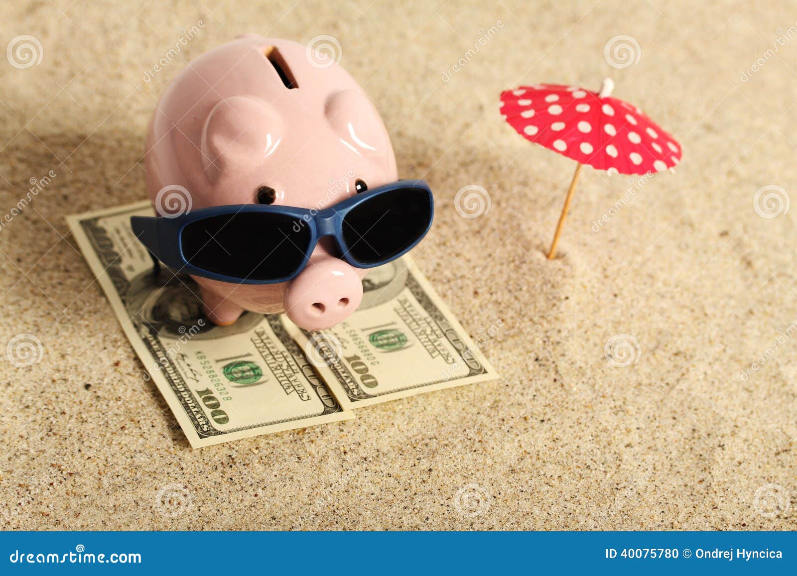 summer piggy bank standing on towel from greenback hundred dollars with sunglasses on the beach and red parasol