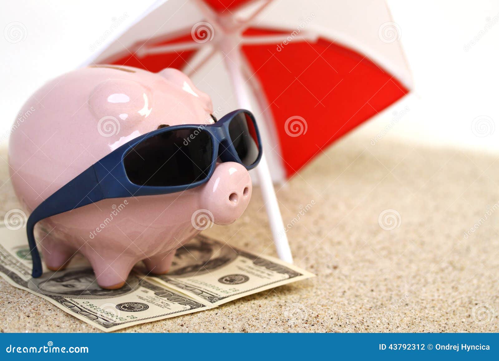 summer piggy bank standing on towel from greenback hundred dollars with sunglasses on the beach sand unter red and white sunshade