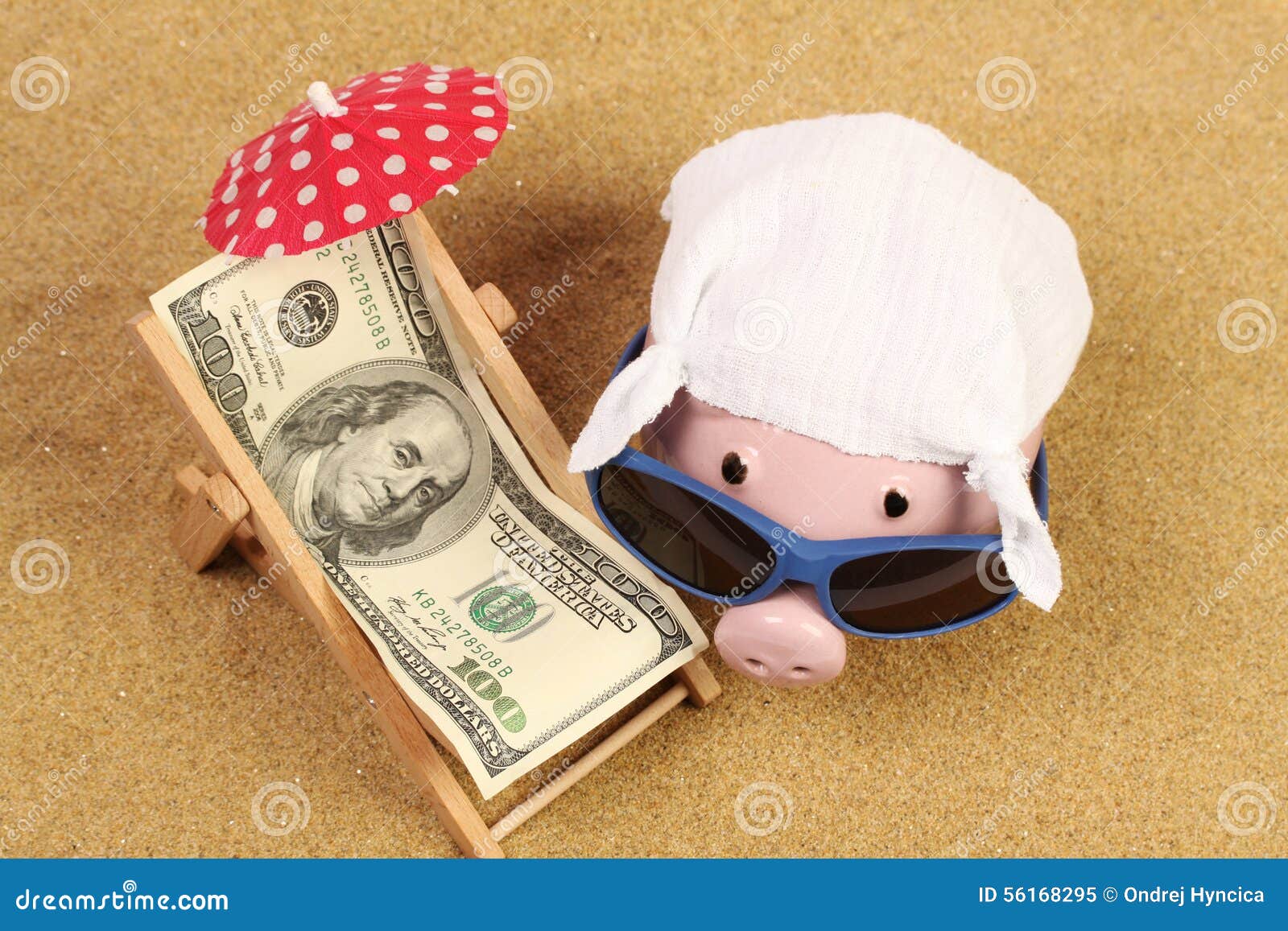 summer piggy bank with sunglasses and hankie next to beach chair with towel from greenback hundred dollars and red parasol on sand