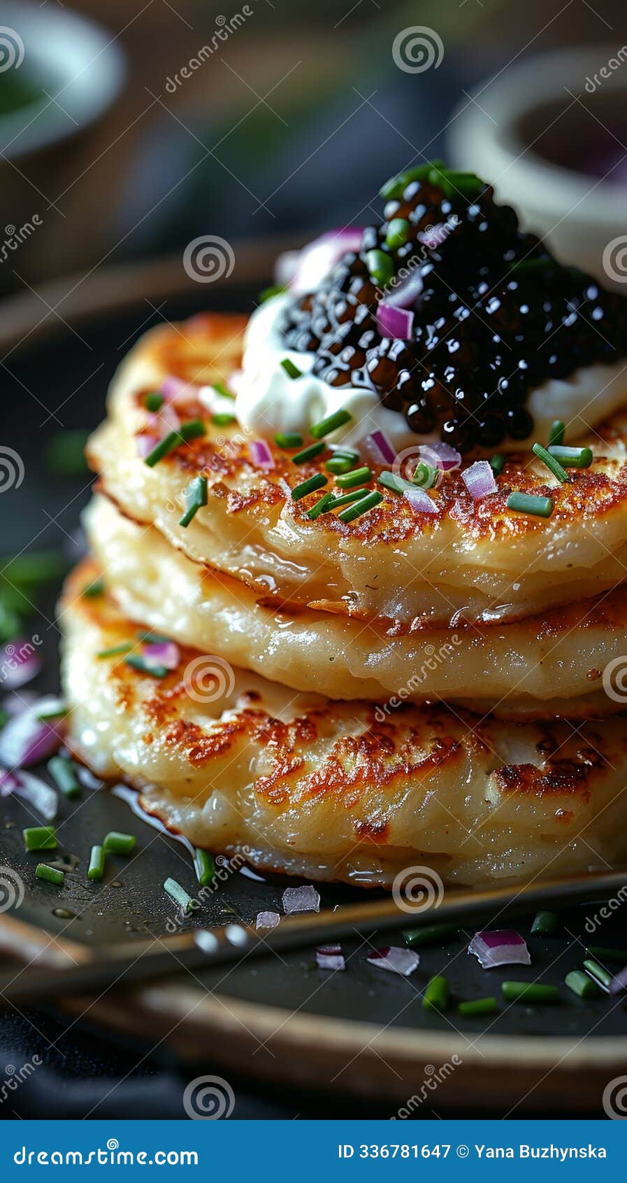 a sumptuous plate featuring golden, fluffy pancakes topped with crÃÂ¨me fraÃÂ®che, caviar, finely chopped red onion, and green