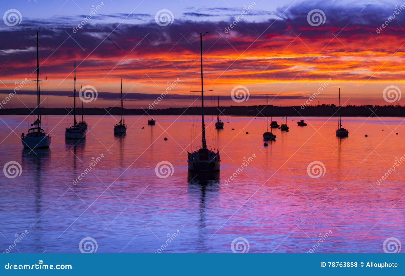 The Sun ajusta-se sobre o porto de Poole em Dorset no jett do cais de Hamworthy. As cores profundas emanam do por do sol, nuvens illuminating e os mares calmos de Poole abrigam em Rockley