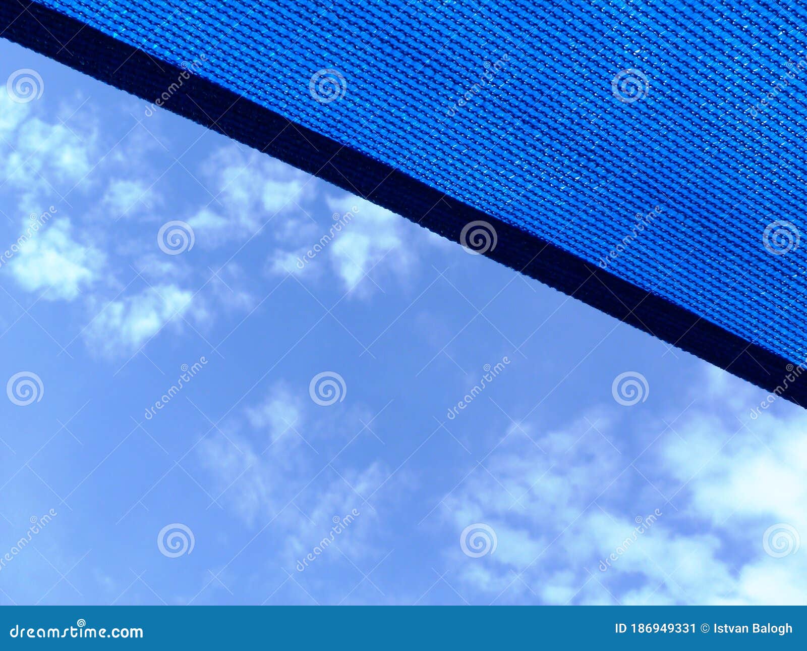 sun sail. loosely weaved blue fabric sun shade material spanning over terrace area. blue sky and cluds