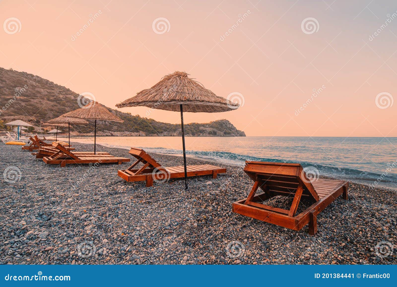 sunbeds and sun umbrellas await vacationers on the shingle beach at ovabuku beach on the datca peninsula in turkey.