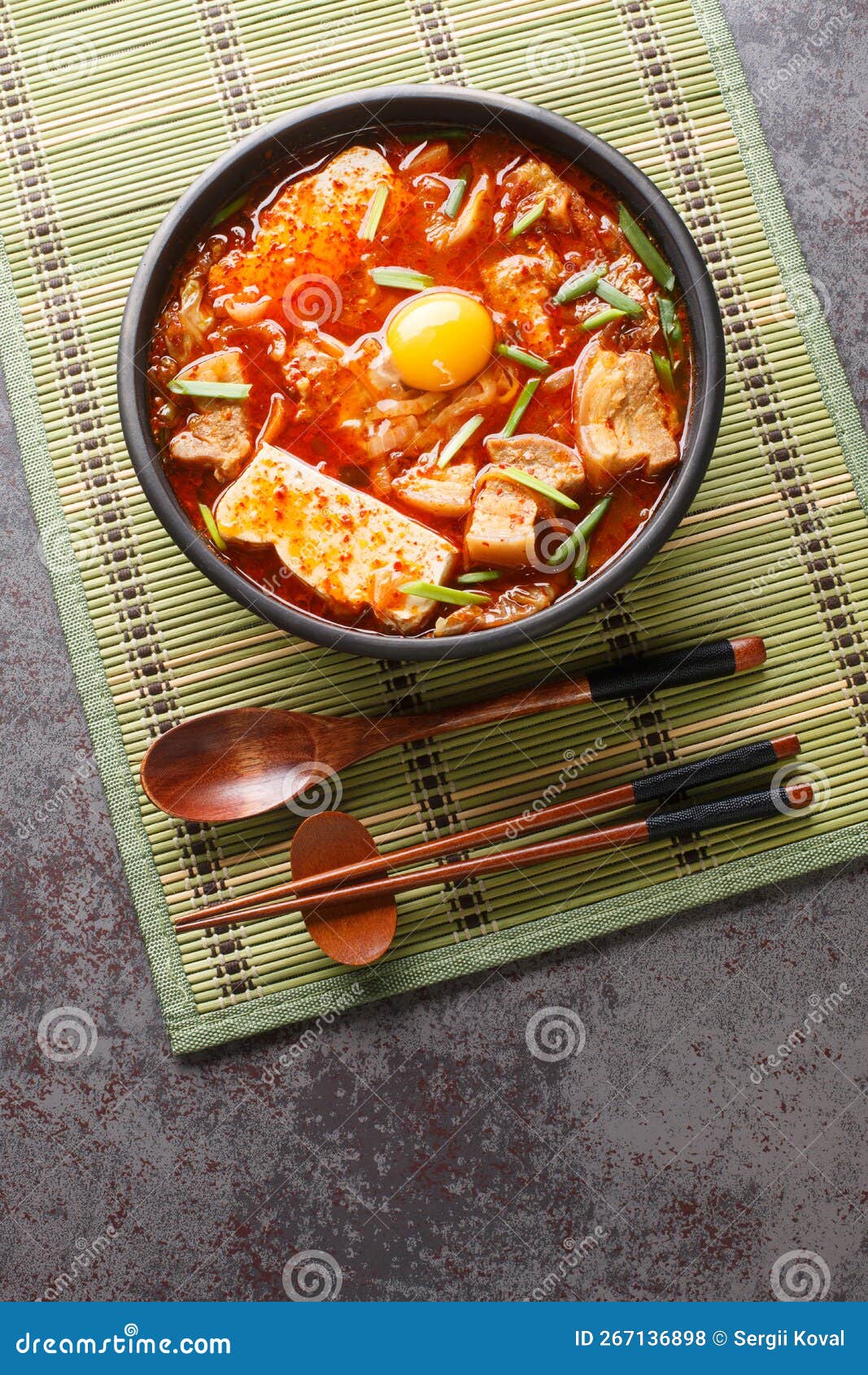 sundubu jjigae is a korean stew made with soft tofu, kimchi, pork belly, onion and spices closeup on the bowl. vertical top view