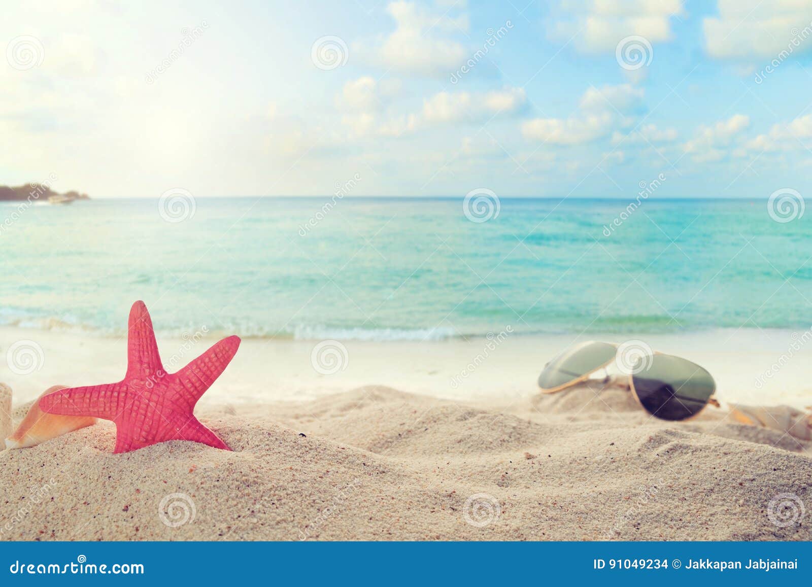 sunglasses on sandy in seaside summer beach with starfish, shells, coral on sandbar and blur sea background
