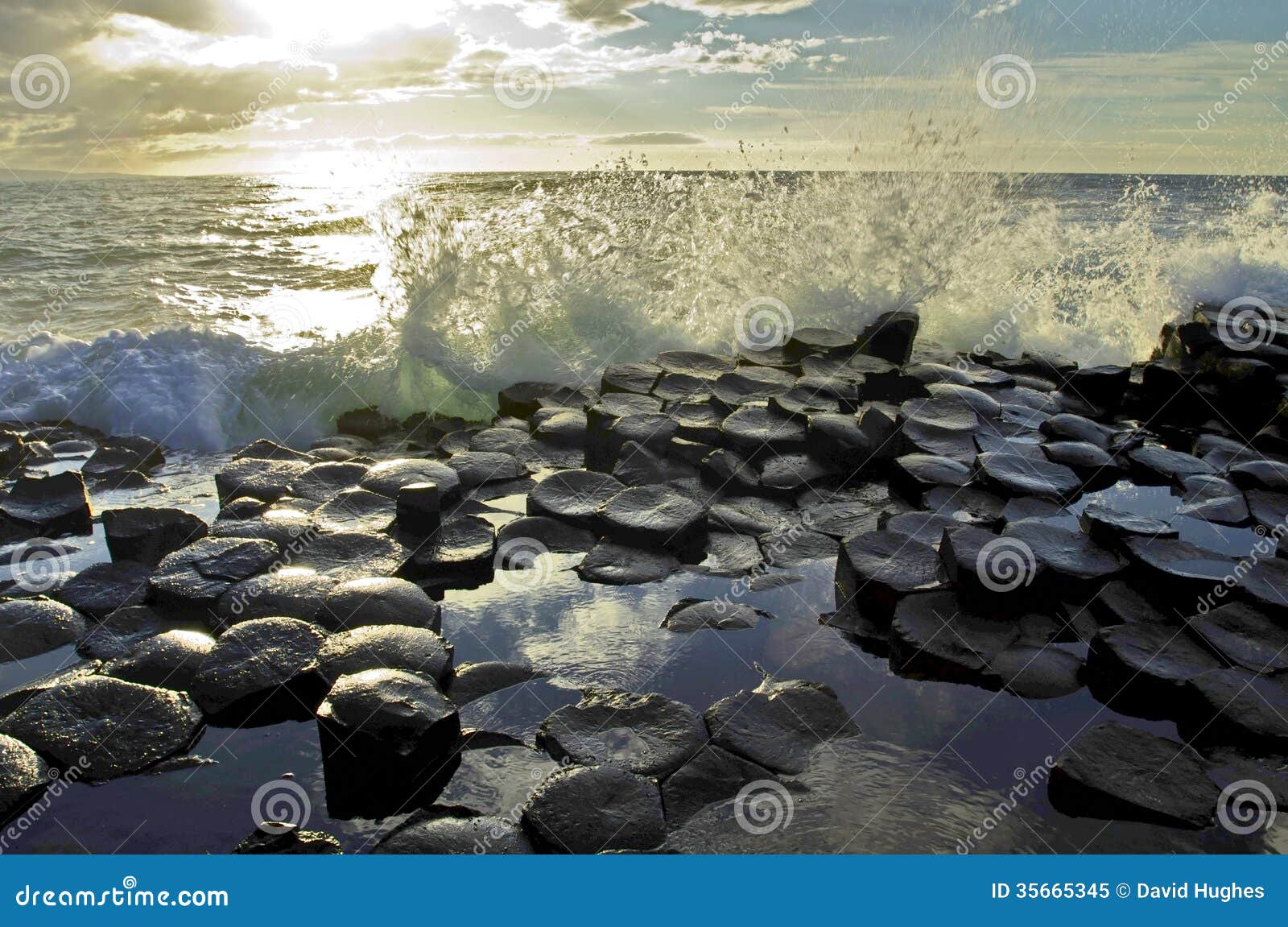 sunlight highlighting waves crashing onto the hexagonal basalt slabs of giants causeway