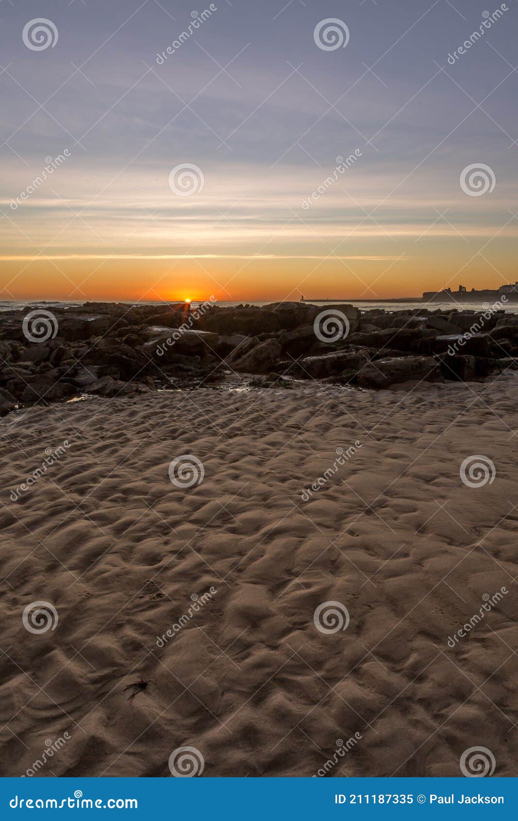 sunrise on tynemouth`s longsands beach as the sun appears on the horizon over the rocks