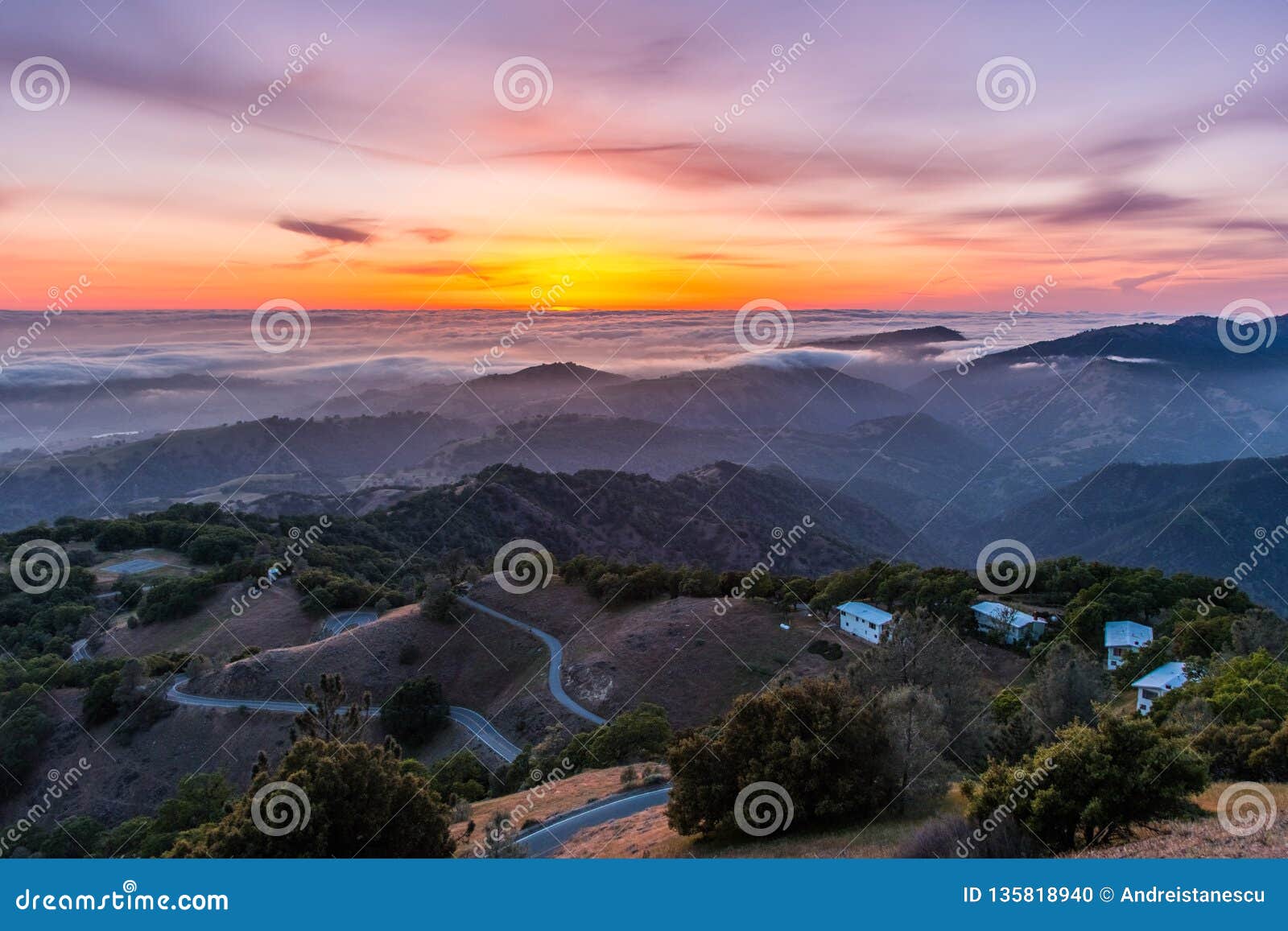 sunset afterglow over a sea of clouds; winding road descending through rolling hills in the foreground; mt hamilton, san jose,