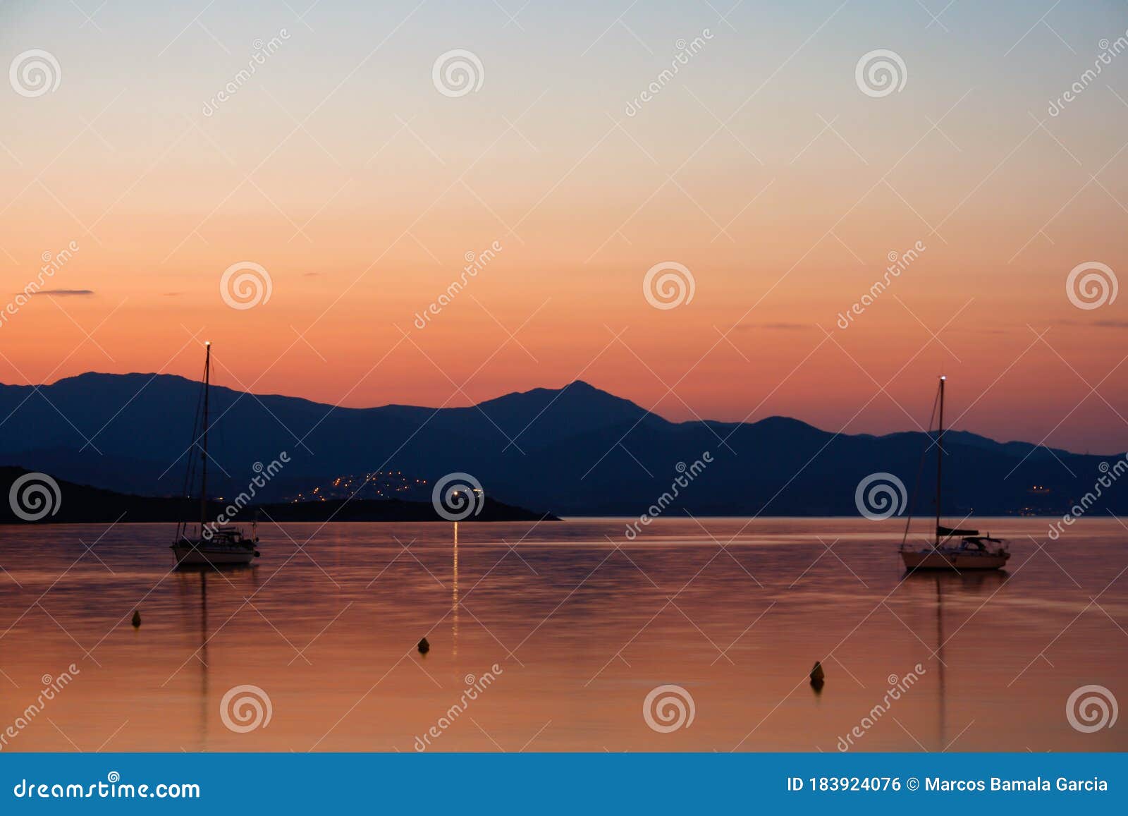 sunset landscape of a bay with two sailboats with the mountains behind.