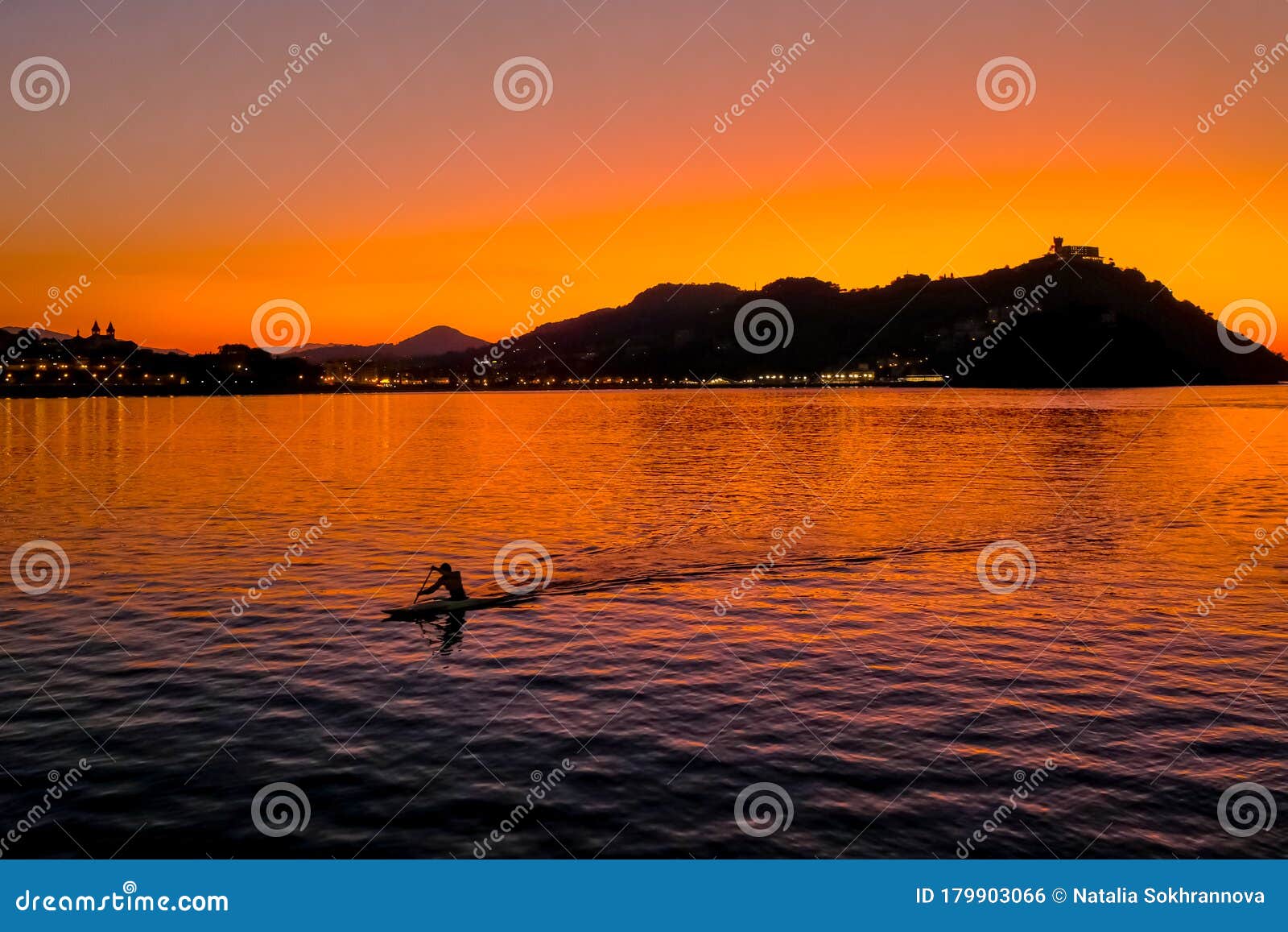 sunset on mount igueldo and and man with a paddle in koyak in donosti san sebastian, basque country, northern spain