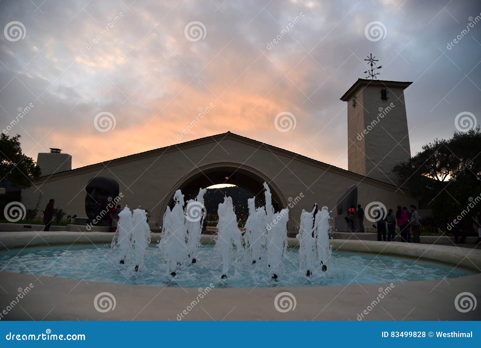 Sunset view in Napa Valley, fountain. Sunset view in Napa Valley with golden orange clouds above undulating mountain top, pond with fountains and Robert Mondavi Winery building in foreground.