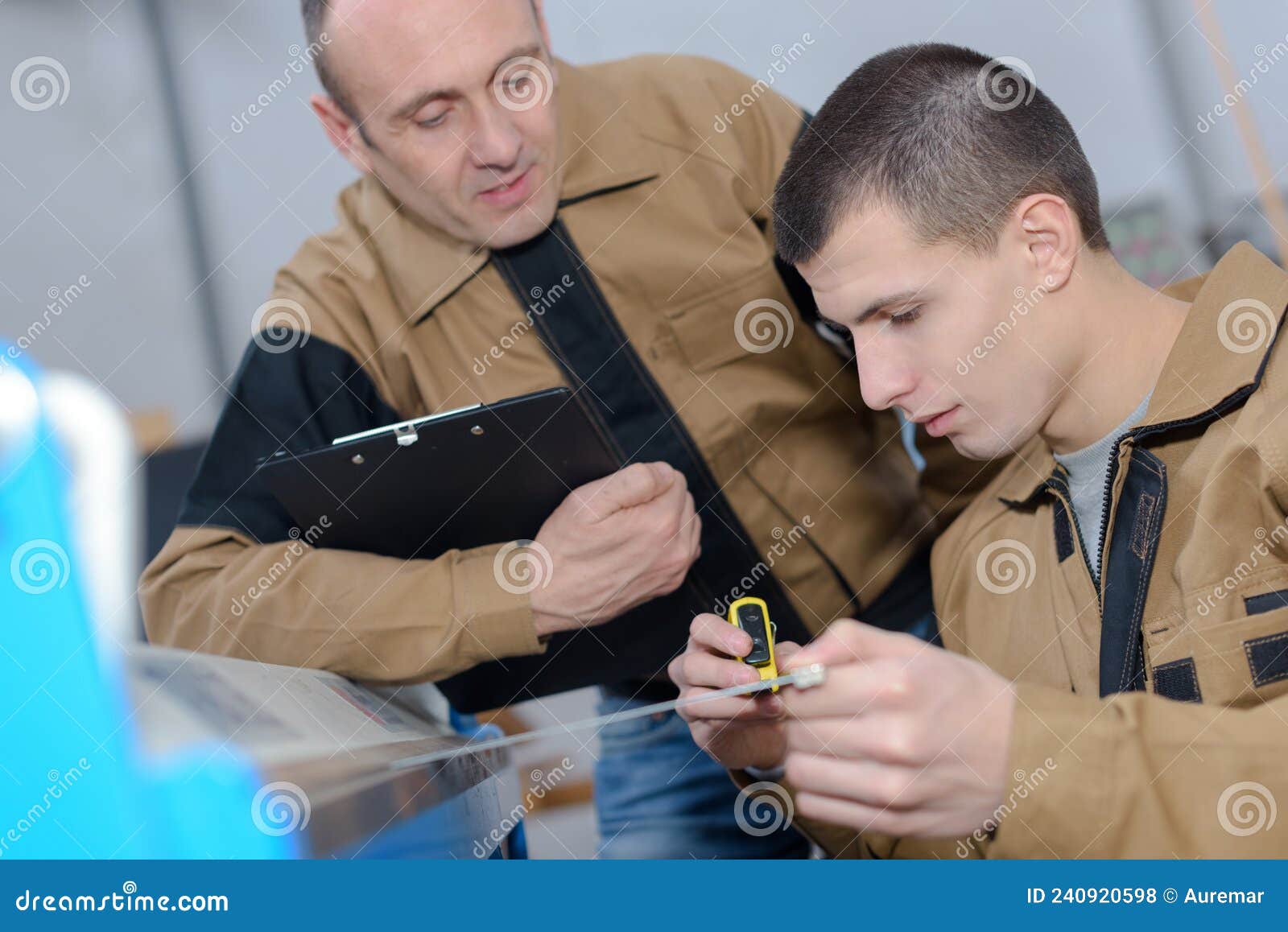 Supervisor with Clipboard Observing Apprentice Using Tape Measure Stock