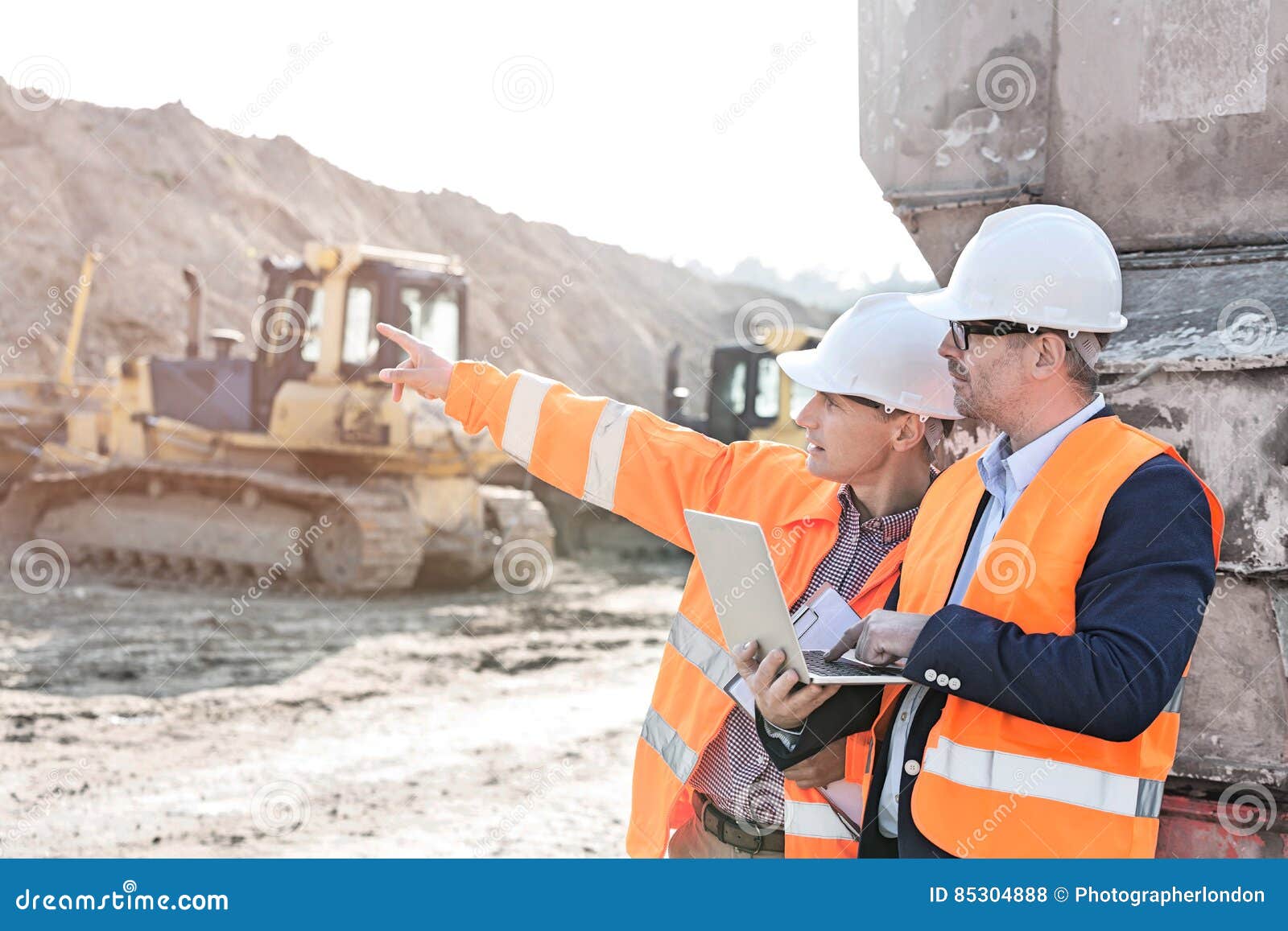 supervisor showing something to coworker holding laptop at construction site