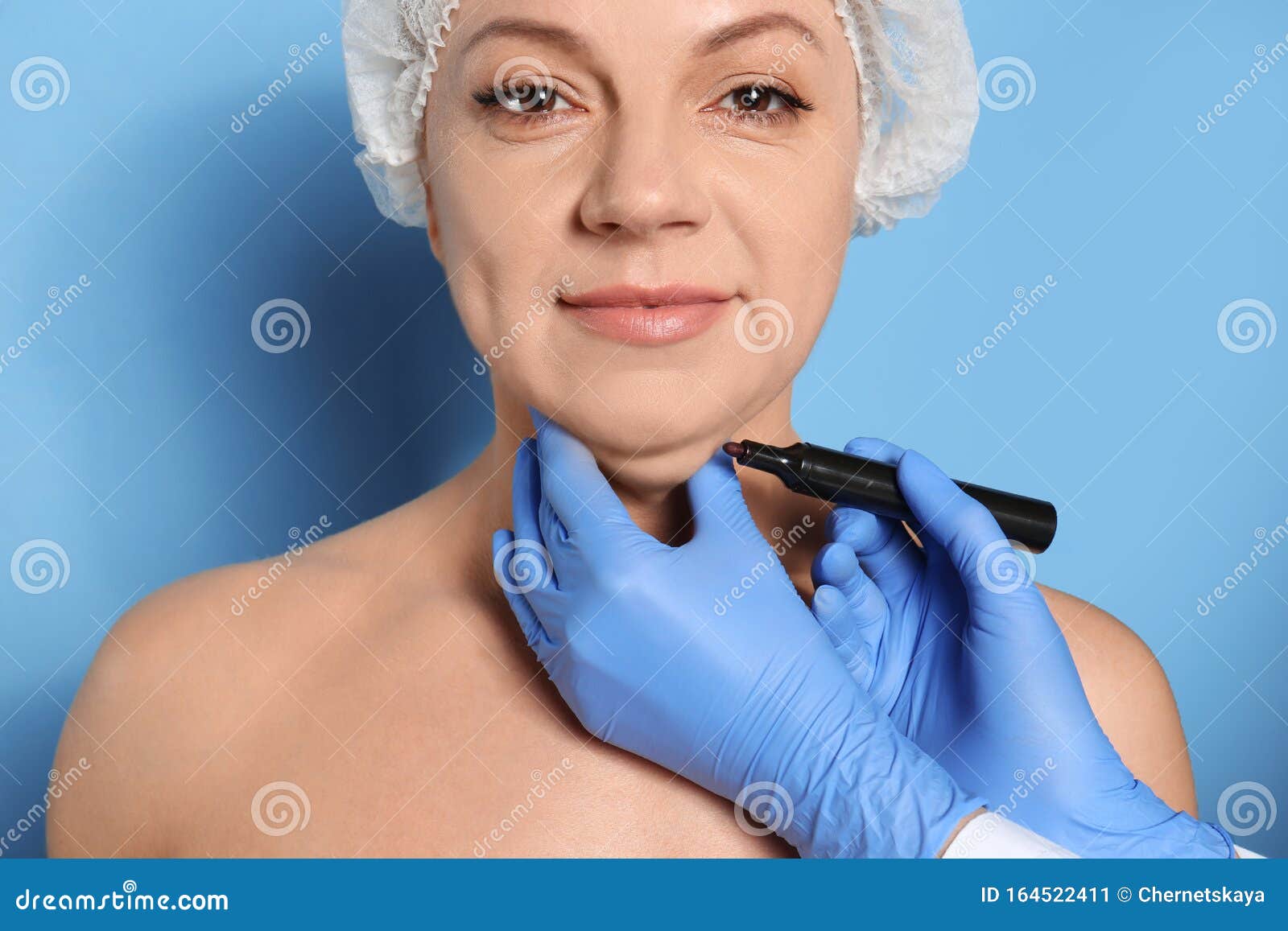surgeon with marker preparing woman for operation against background. double chin removal