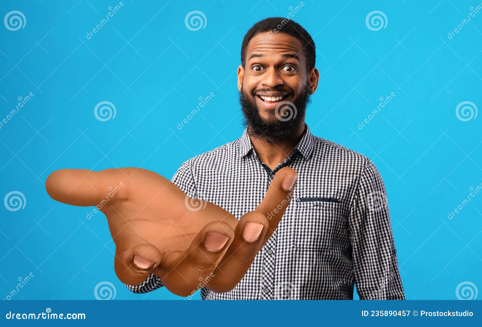 surprised young black man standing with big outstretched hand on blue studio background, mockup for your product
