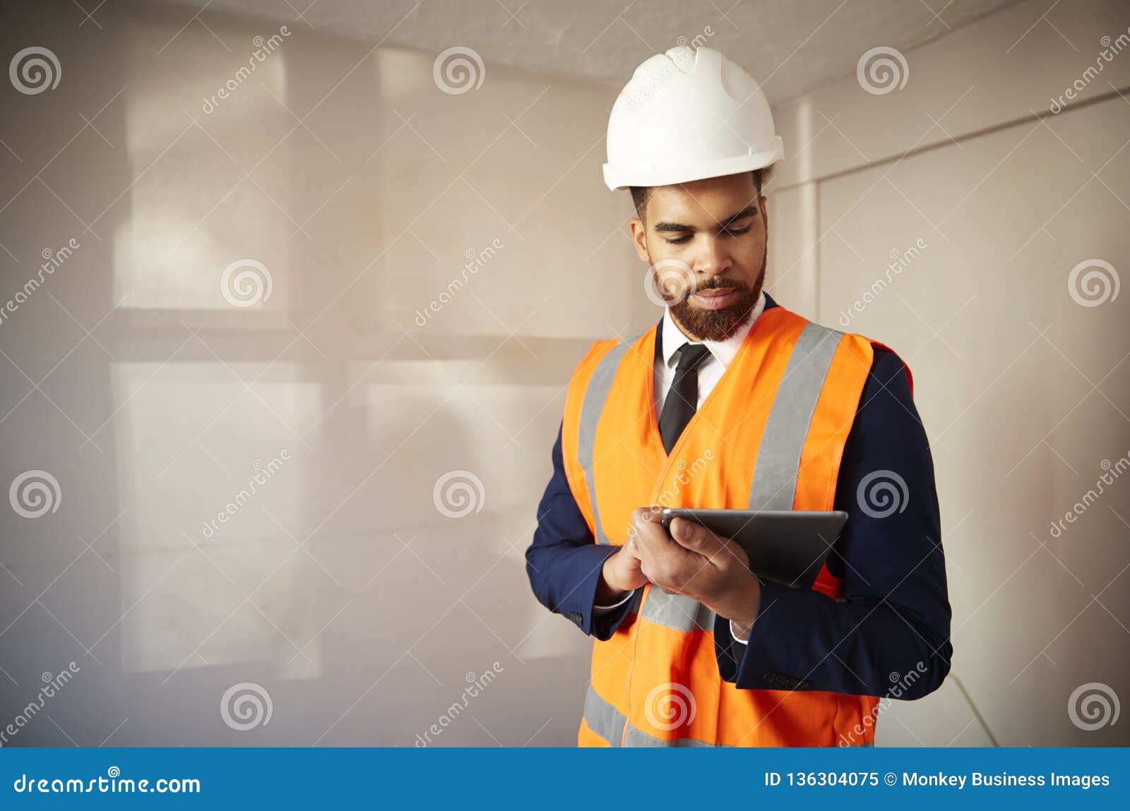 surveyor in hard hat and high visibility jacket with digital tablet carrying out house inspection