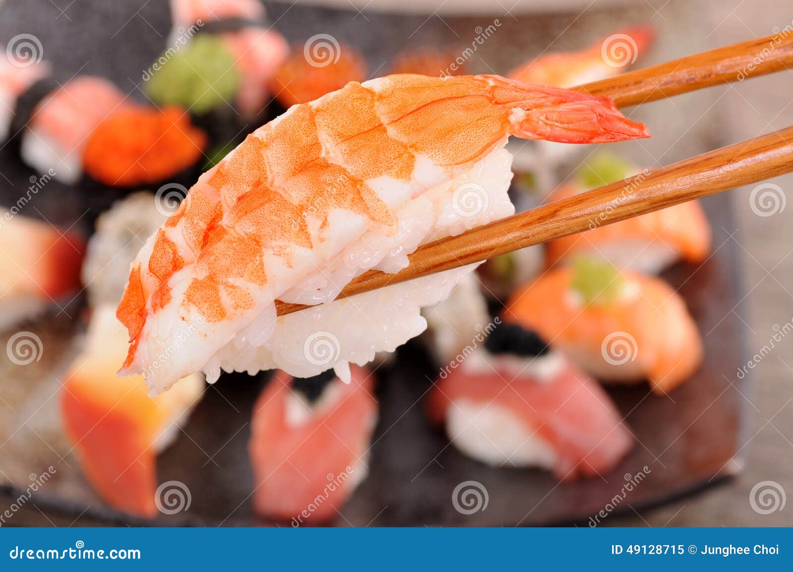 Sushi de la gamba sostenido por los palillos. El sushi de la gamba se sostuvo al lado de los palillos del fondo del disco clasificado del sushi