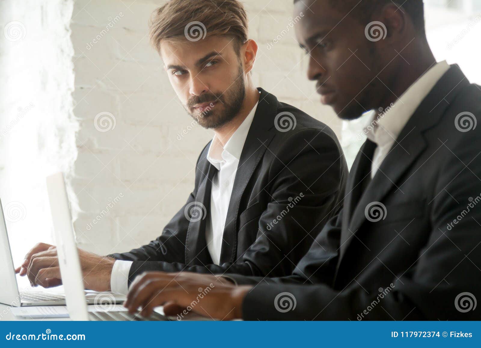 suspicious caucasian worker looking madly at busy black colleagu