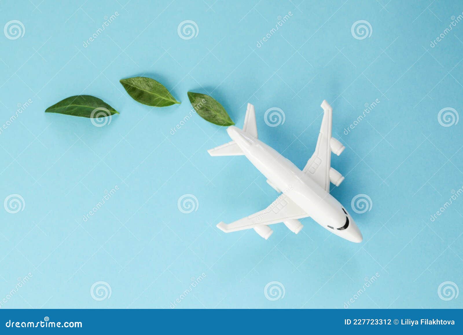 sustainable aviation fuel. white airplane model, fresh green leaves on blue background. green biofuel for aviation