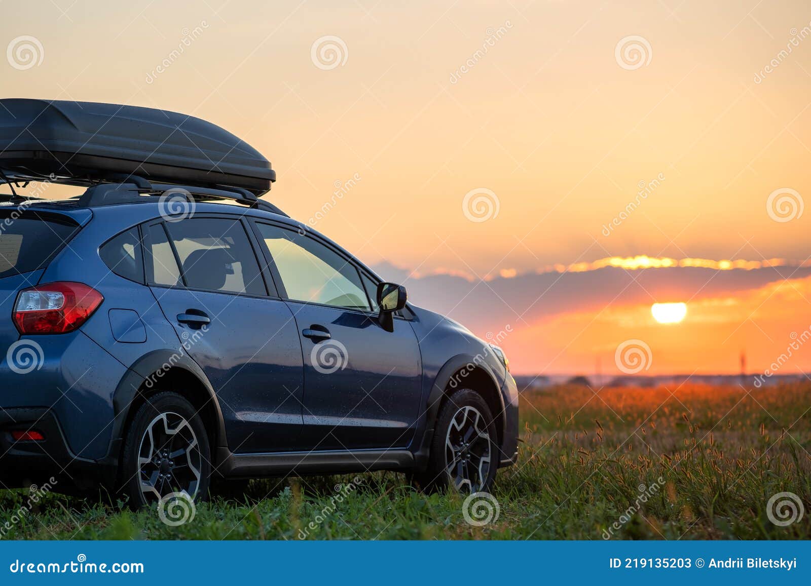 suv car with roof rack luggage container for off road travelling parked at roadside at sunset. road trip and getaway concept