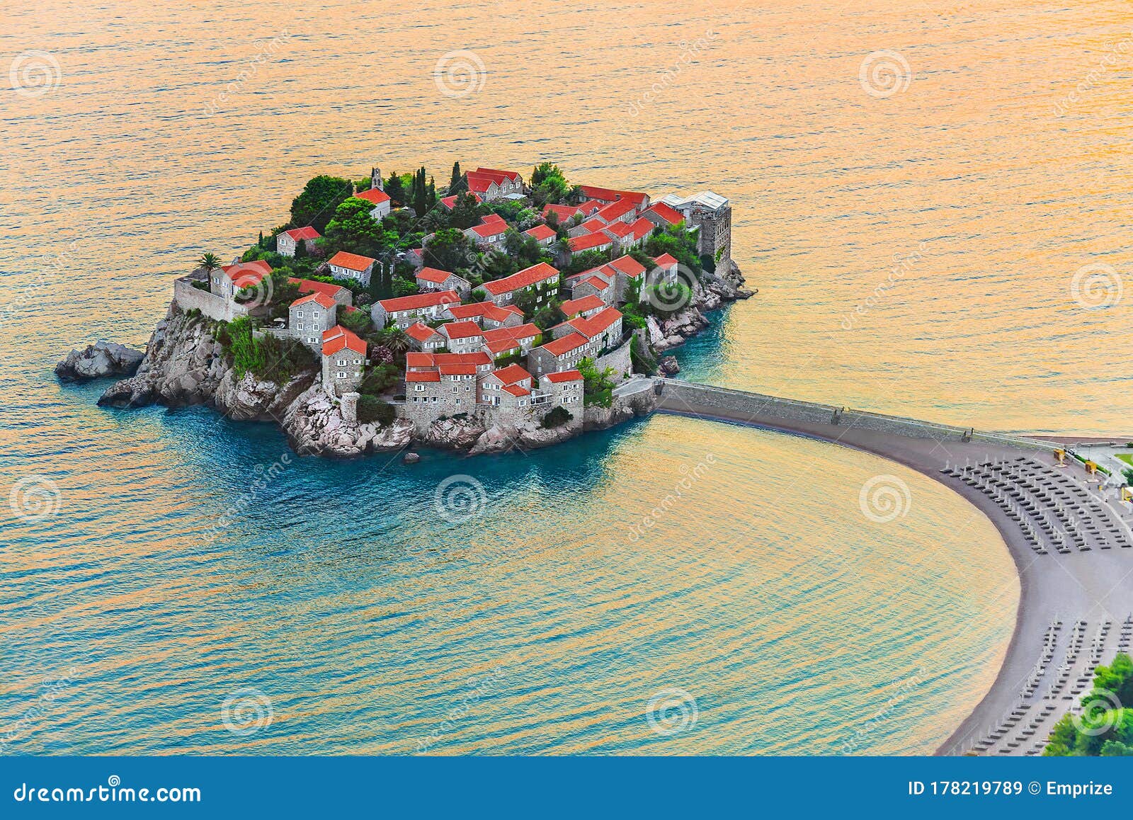 sveti stefan small island with red-tiled roofs, green trees and beautiful sandy beach with sunbeds on the adriatic coast of