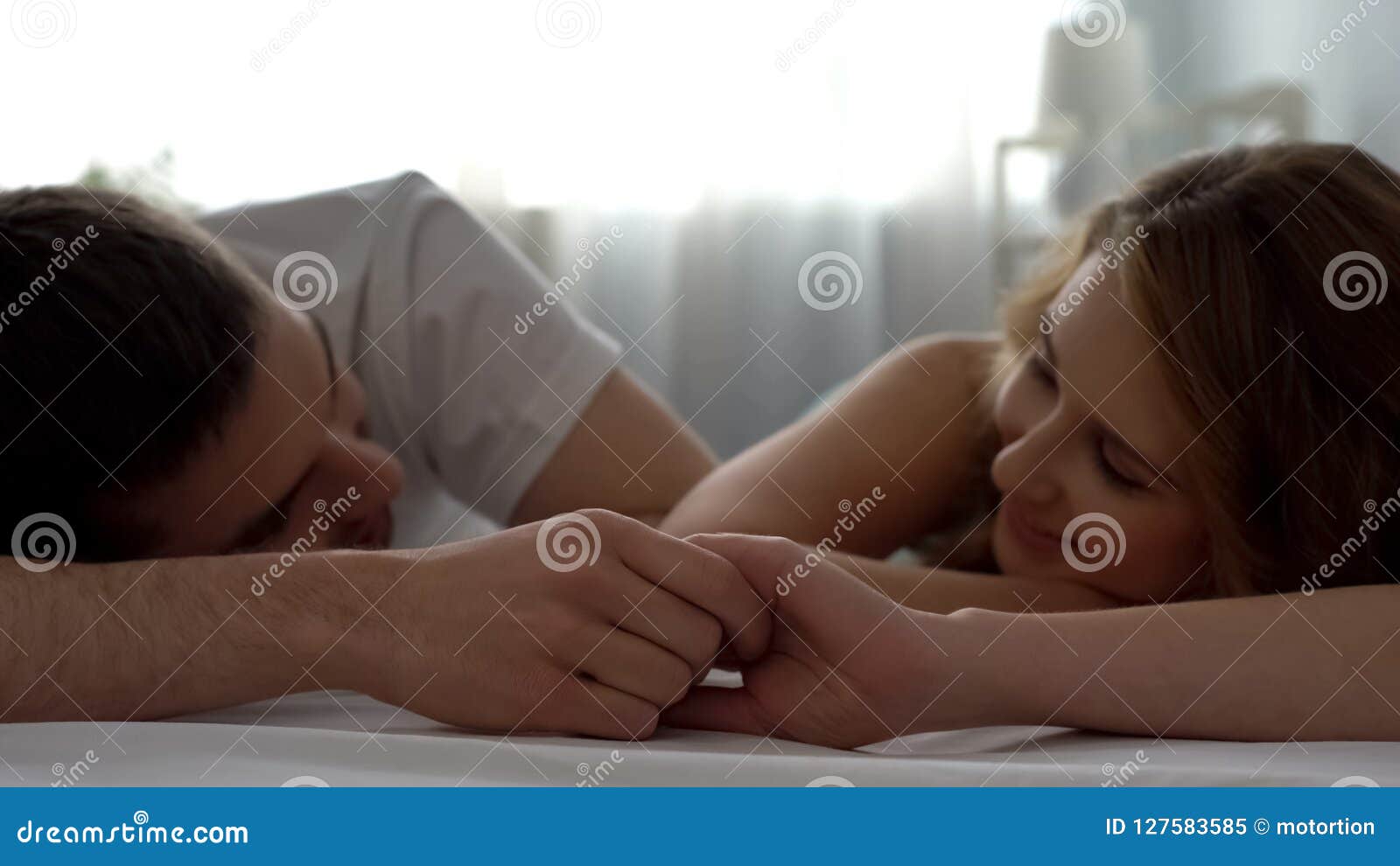 sweet couple looking at each other with love, holding hands in bed, closeness