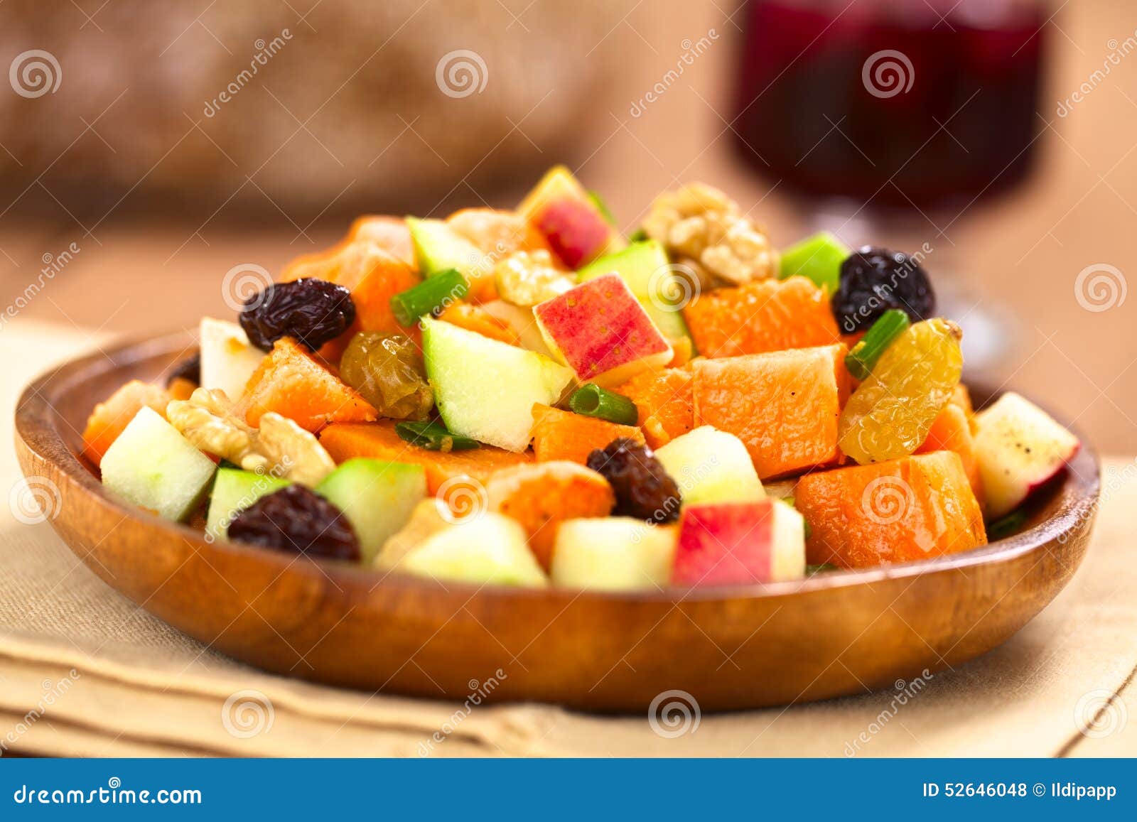 Sweet Potato and Apple Salad. Fresh salad made of cooked sweet potatoes, fresh apples, nuts, raisins and shallots on wooden plate with mulled wine in the back (Selective Focus, Focus one third into the salad)