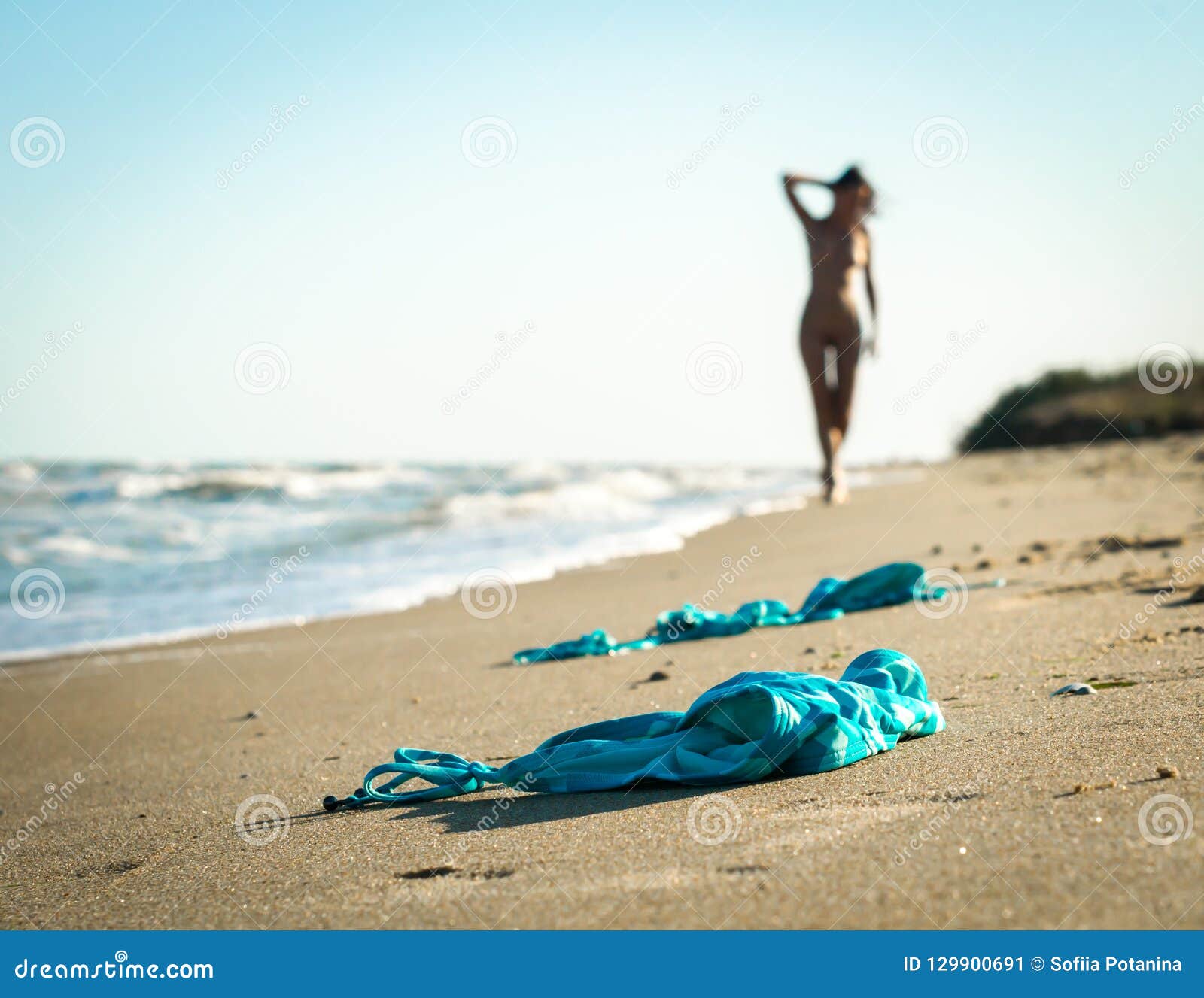 Swimsuit in the Sand on the Beach Near the Sea Surf on the Background of a Naked Female Figure and Blue Sky Stock Image