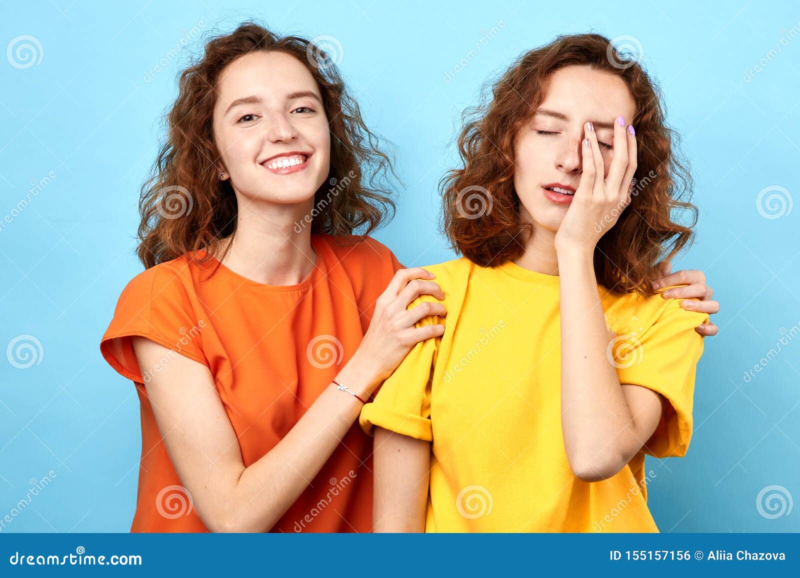 Syster som försöker att lugna ner hennes skriande syster som har några problem. Sister trying to calm down her crying sister who has some problems. woman trying to support her favourite sister in difficult situstion . isolated blue background. studio shot