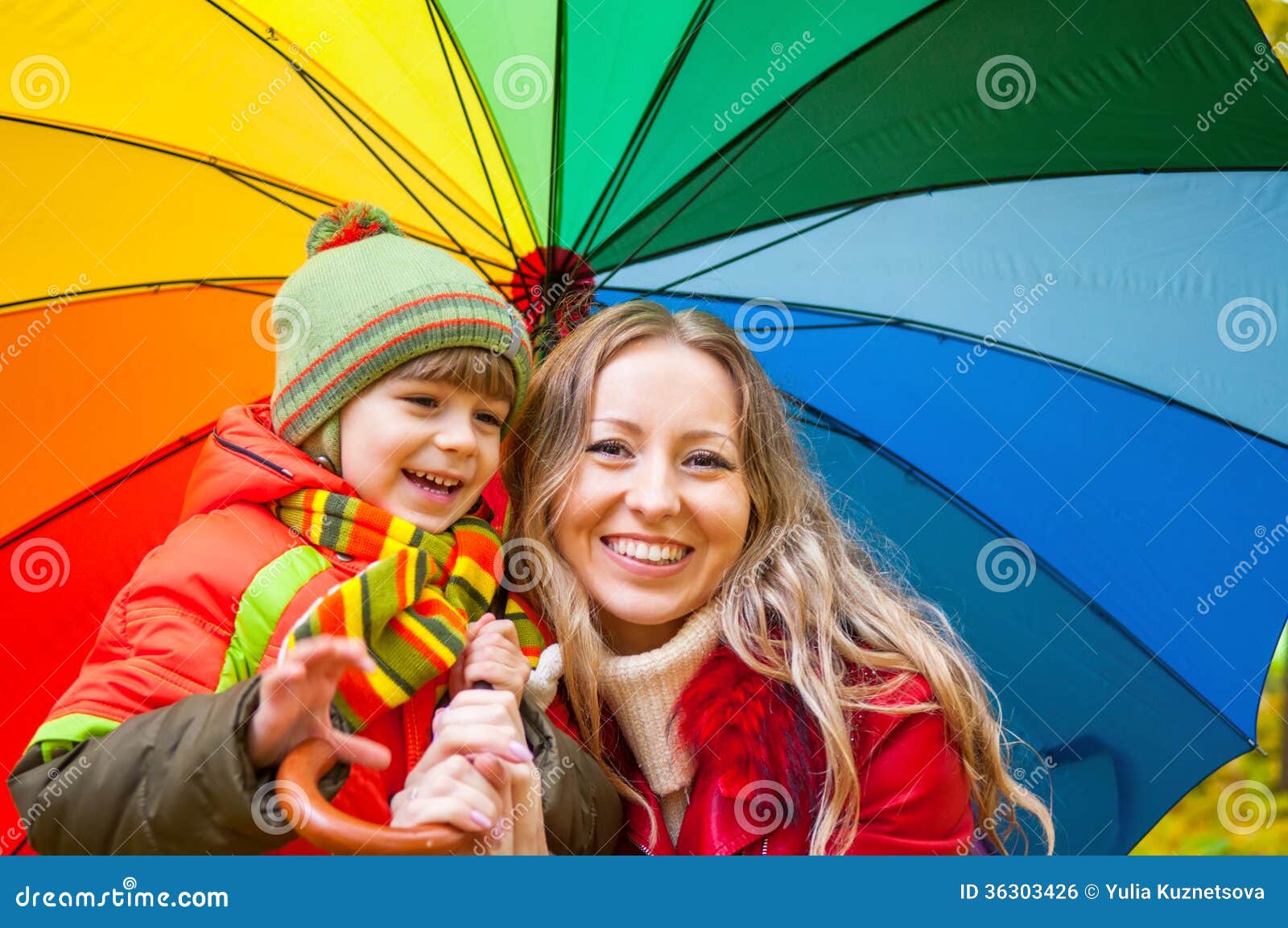 Szczęśliwa rodzina z kolorowym parasolem w jesień parku. Szczęśliwa rodzina z jaskrawym stubarwnym parasolem w jesień parku