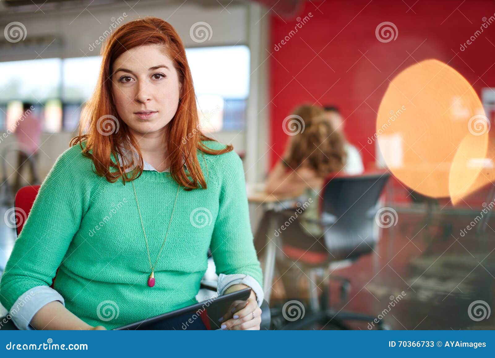 Säkert kvinnligt märkes- arbete på en digital minnestavla i rött idérikt kontorsutrymme. Tillfällig stående av kvinnor för en rödhårig manaffär som använder teknologi i en ljus och solig start med laget i bakgrunden