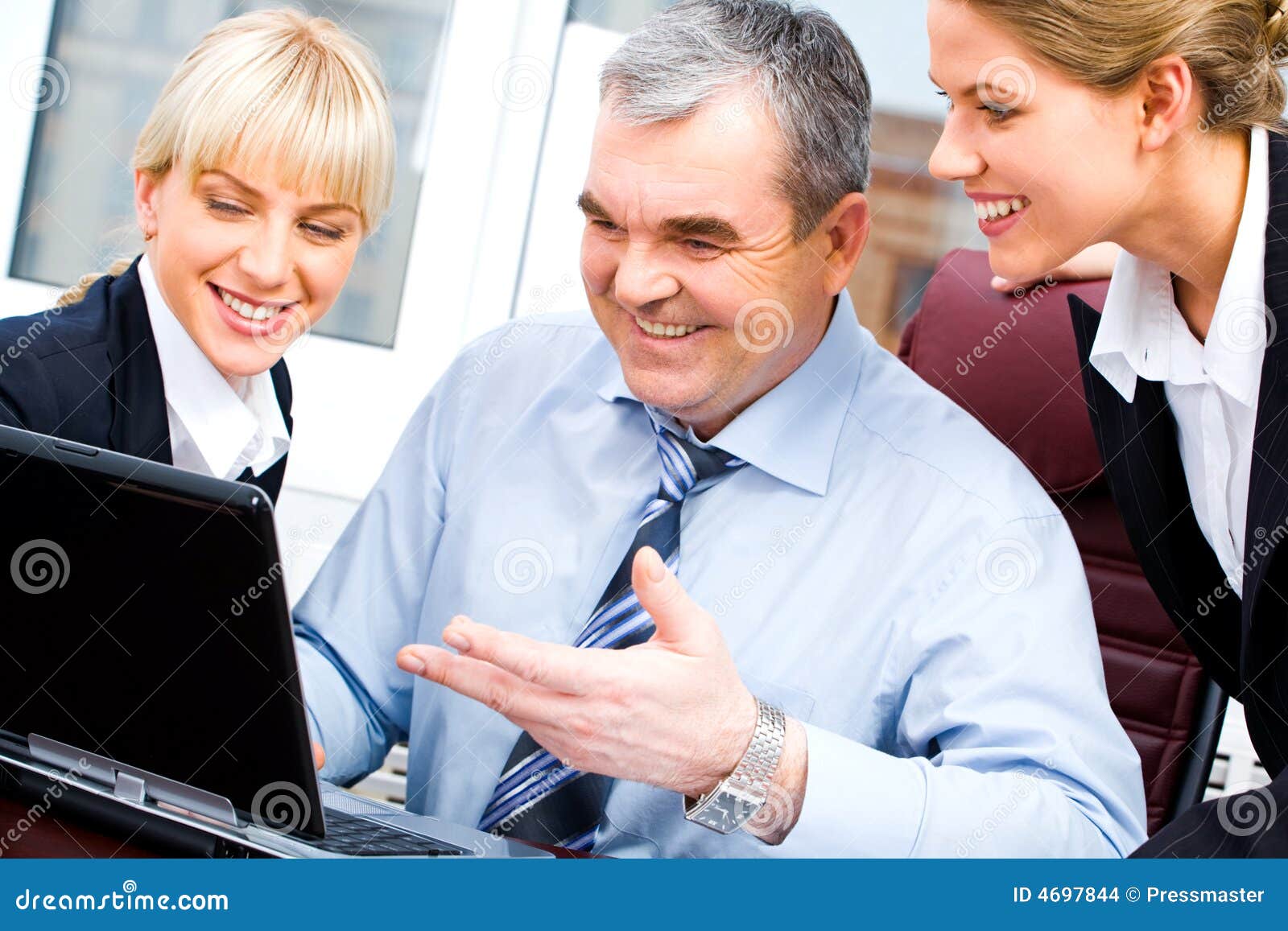 Sócios comerciais felizes. Retrato da saliência sênior e duas das mulheres de negócios novas que olham o monitor do portátil com sorrisos no fundo do indicador do escritório