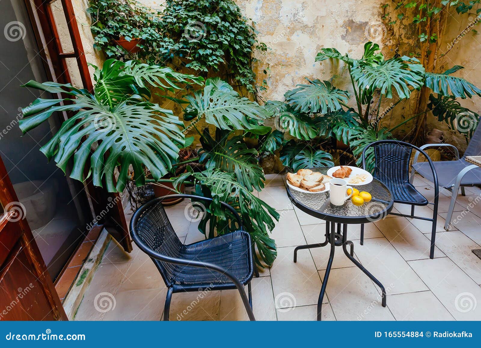 table with breakfast plates in small green courtyard of historical house in mediterranian region. romantic holidays