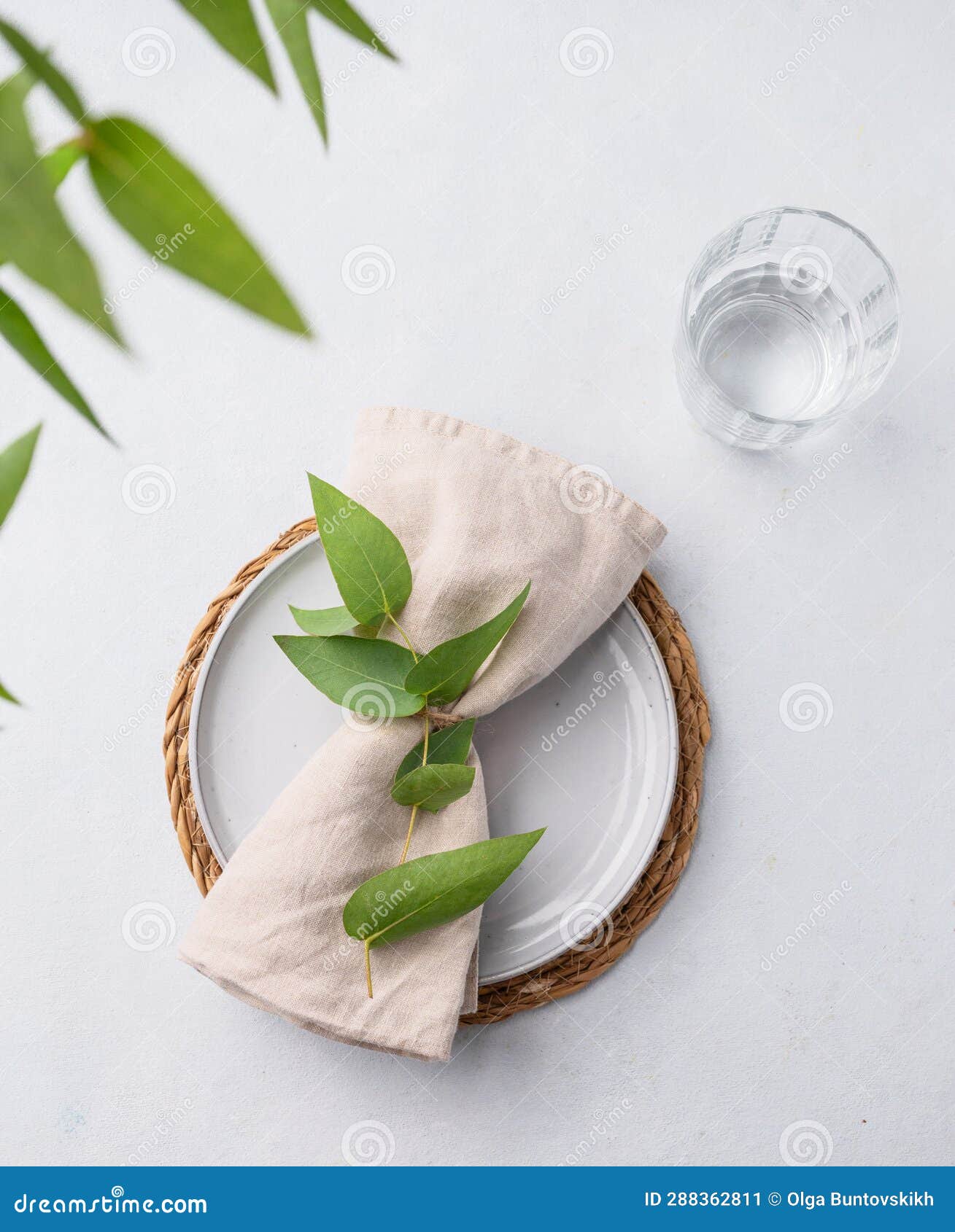 Table Setting with a Blue Plate and a Glass on a Straw Napkin with Eucalyptus Branches on a