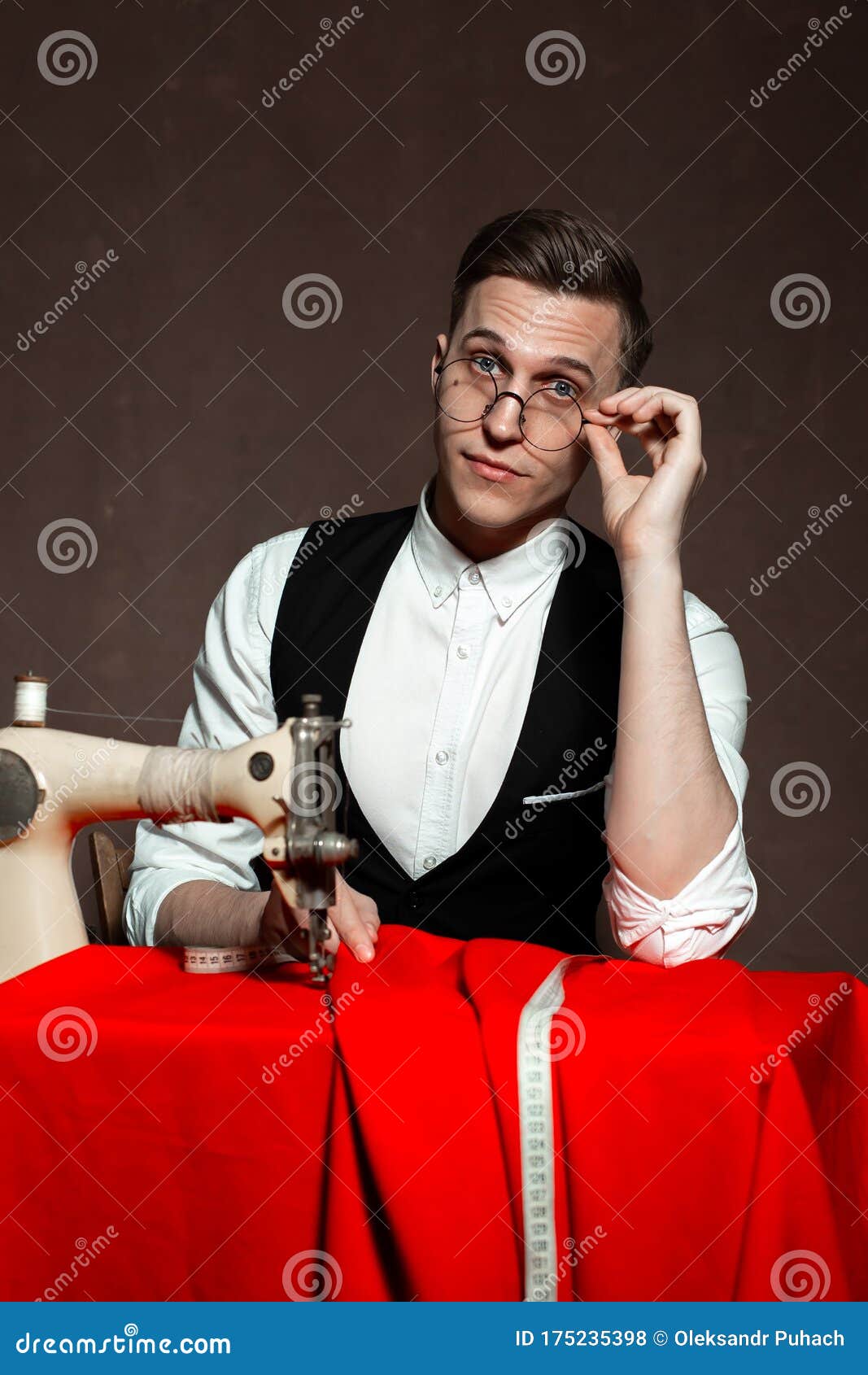 Tailor in Round Glasses Sits at a Table with a Sewing Machine Stock