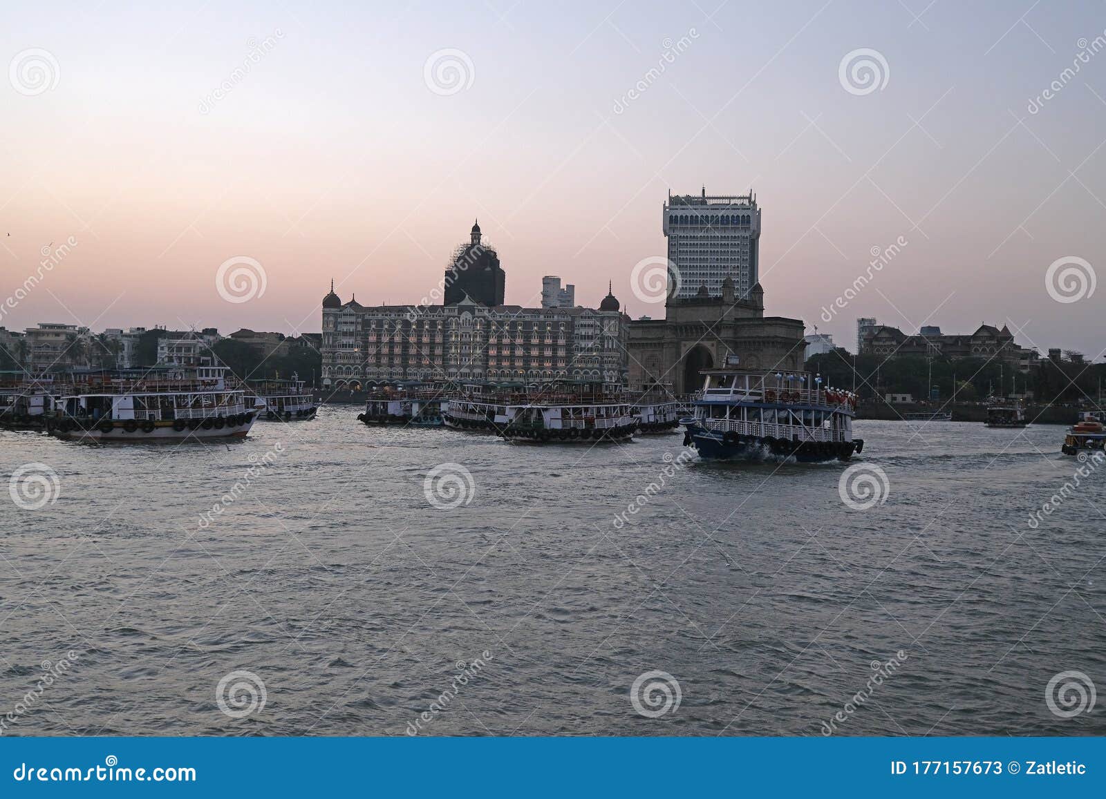 taj mahal hotel, gateway of india and tourist boats in water of arabian sea on sunset in mumbai