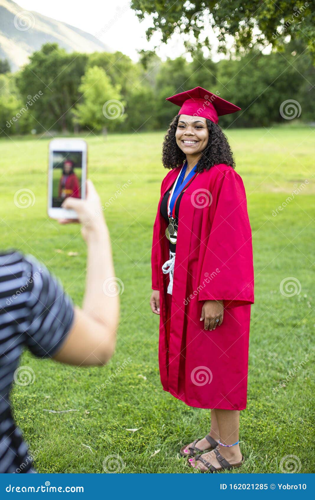 taking a smartphone photo of a recent high school graduate in her cap and gown