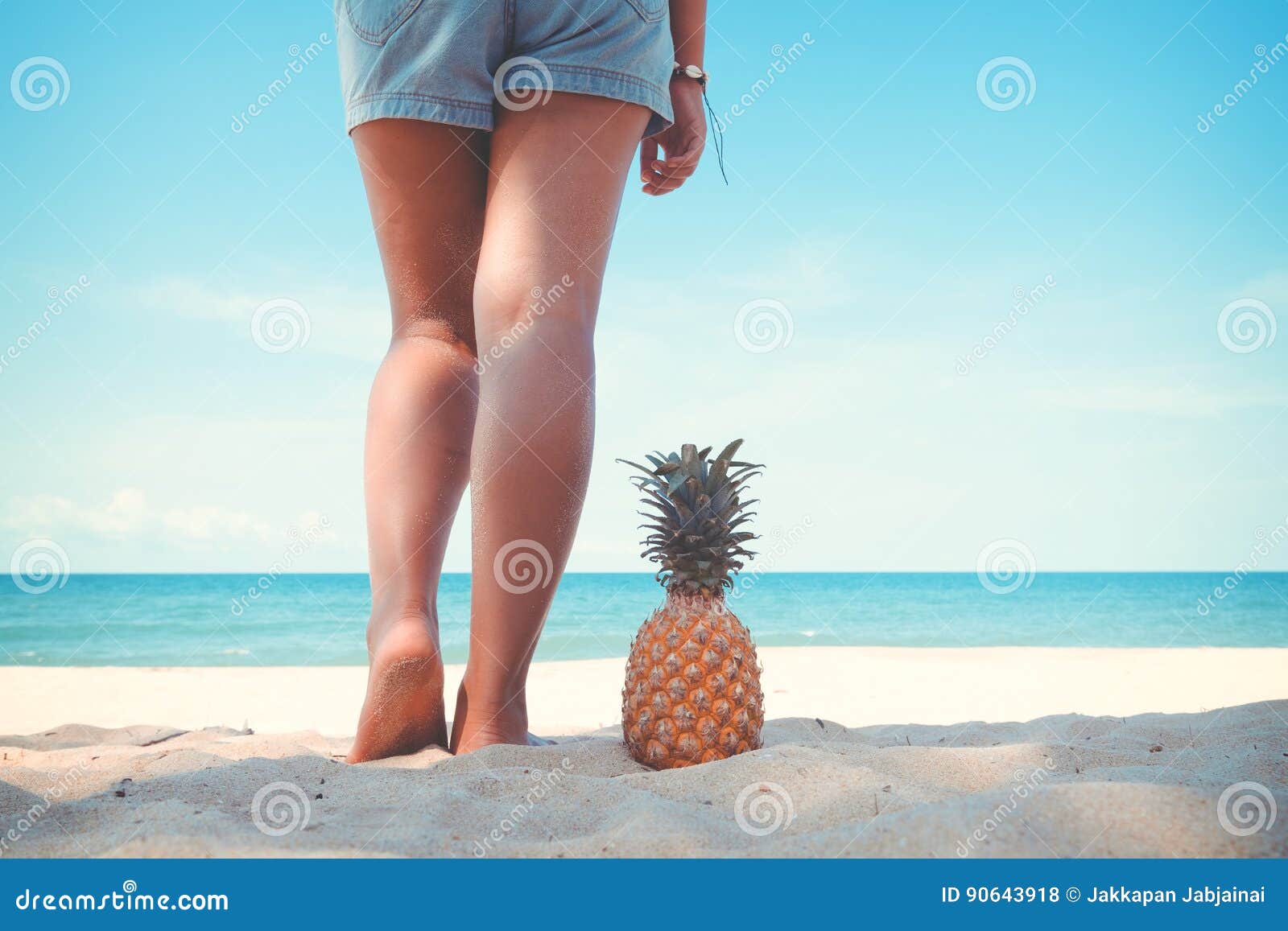 Tanned Legs Of Young Woman Standing With Pineapple At Tropical Beach In 
