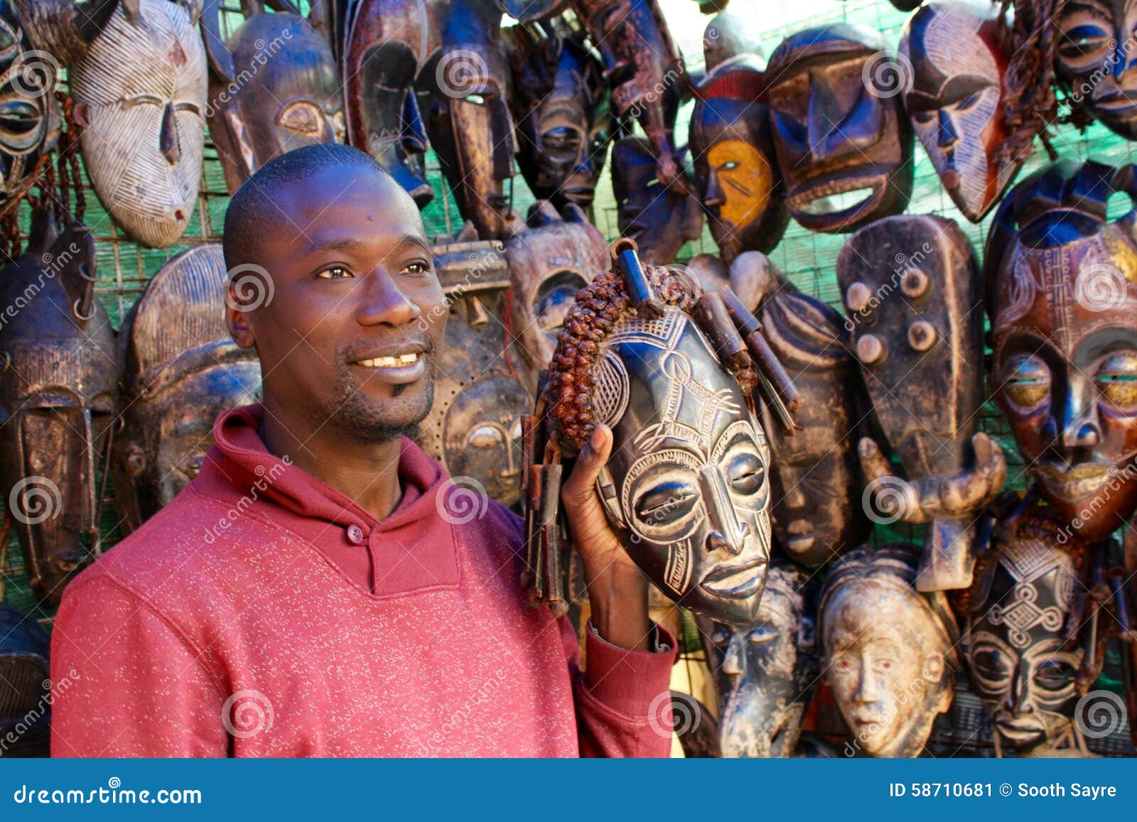Targowy mężczyzna z maskami. Czarnego Afrykanina mężczyzna ono uśmiecha się wśród plemiennych rzeźb i odzieży przy Greenmarket, Kapsztad, Południowa Afryka