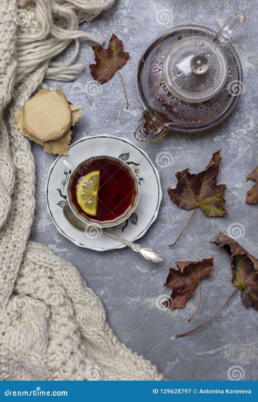 Composition en vie toujours et en concept Tasse avec le thé noir et le citron et la soucoupe, la cuillère, la gelée dans le pot, les feuilles d'érable et l'écharpe tricotée près, un fond gris