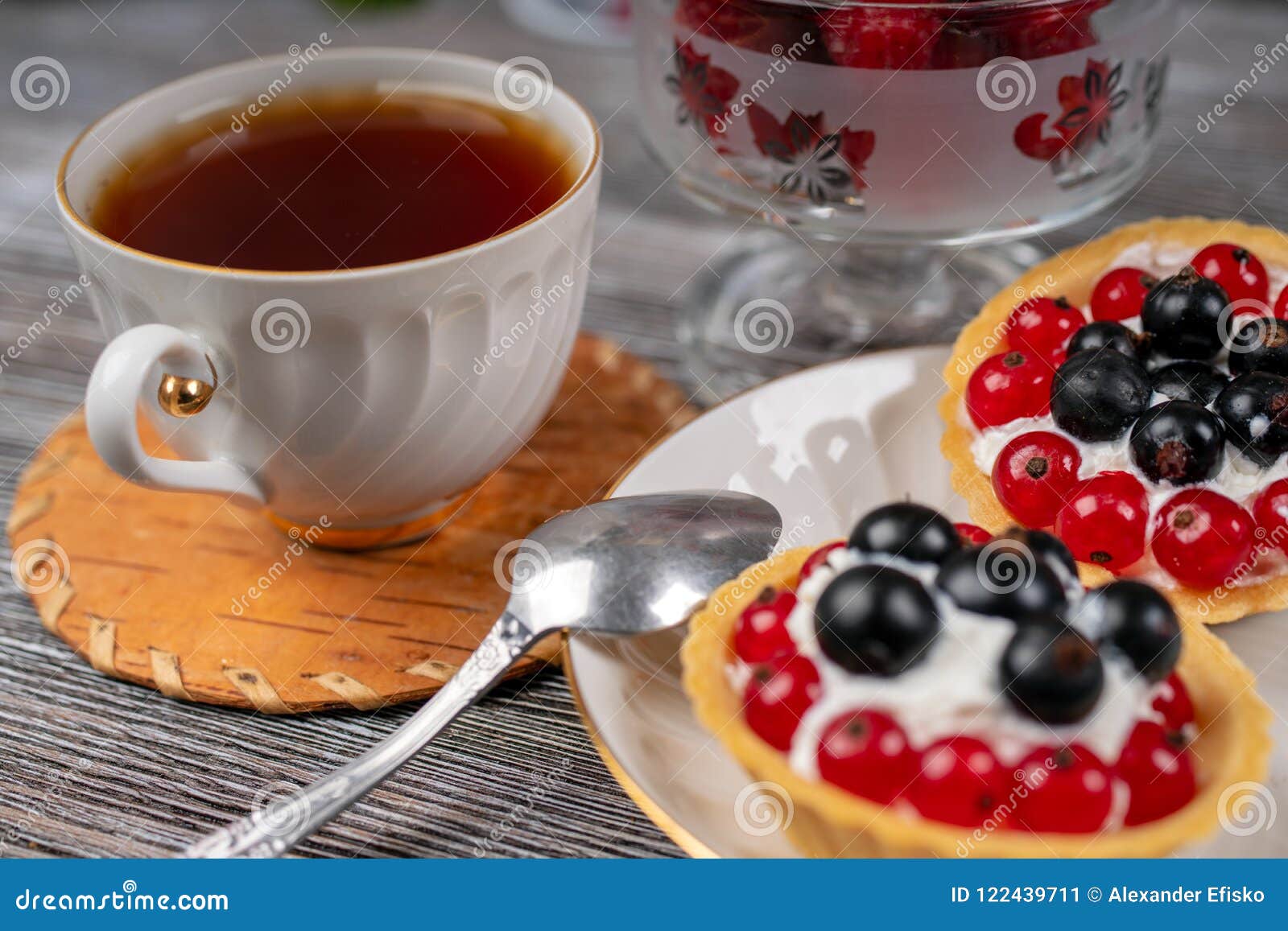 Tasse Tee und Körbe mit Sahne und Korinthe. Schwarzweiss-Stämme von Birken auf dem Hintergrund von grünen Blättern