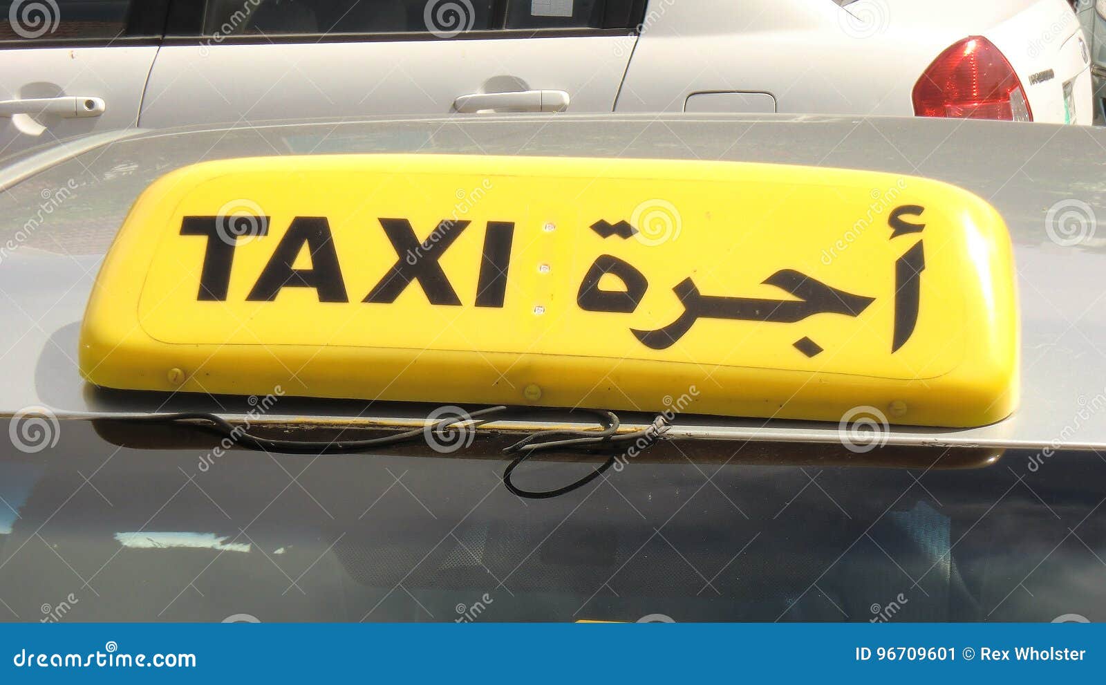 Taxien undertecknar in arabiska och engelska. Ett gult taxitecken på en taxi i Abu Dhabi i både arabiska och engelska språk