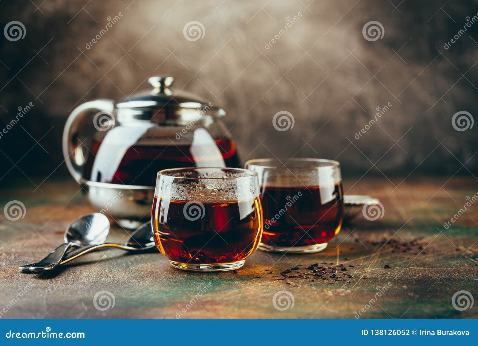 Tetera de cristal transparente con té negro y taza de té vacía