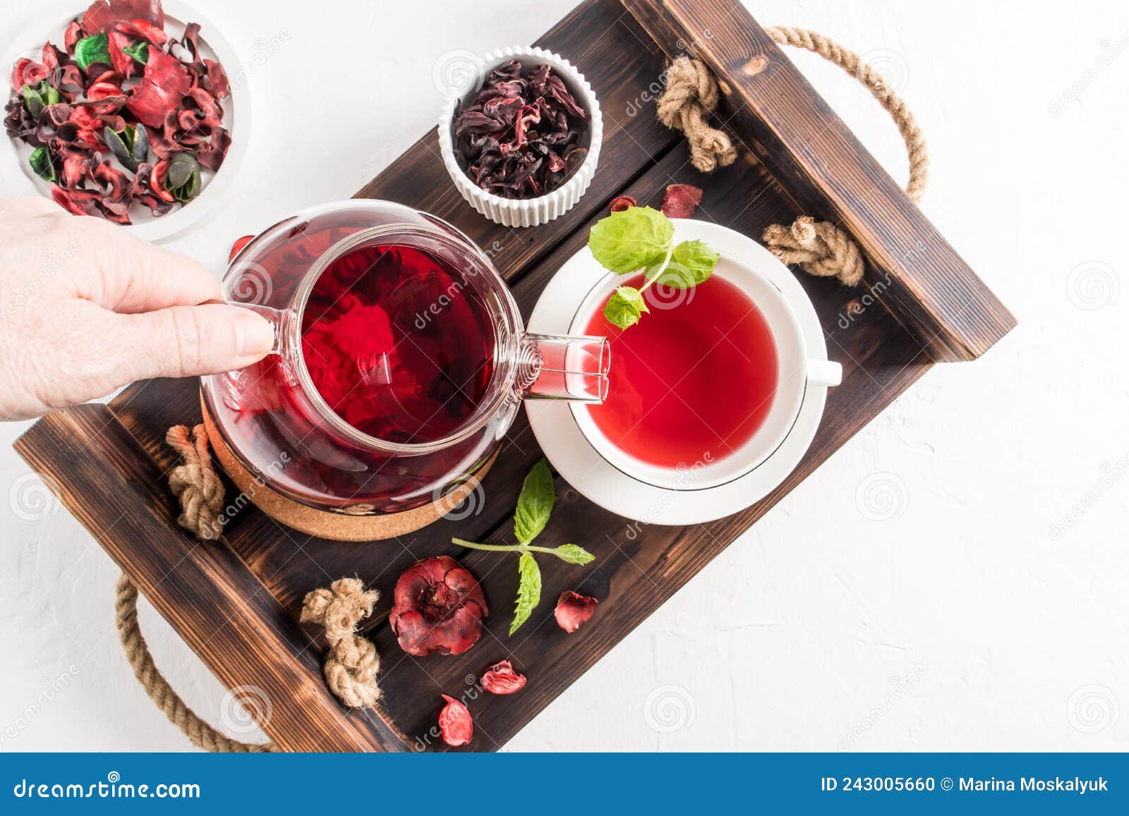 tea ceremonia . a woman`s hand pours fragrant red hibiscus tea into a cup of mint leaves. top view of the wooden tray with mornin