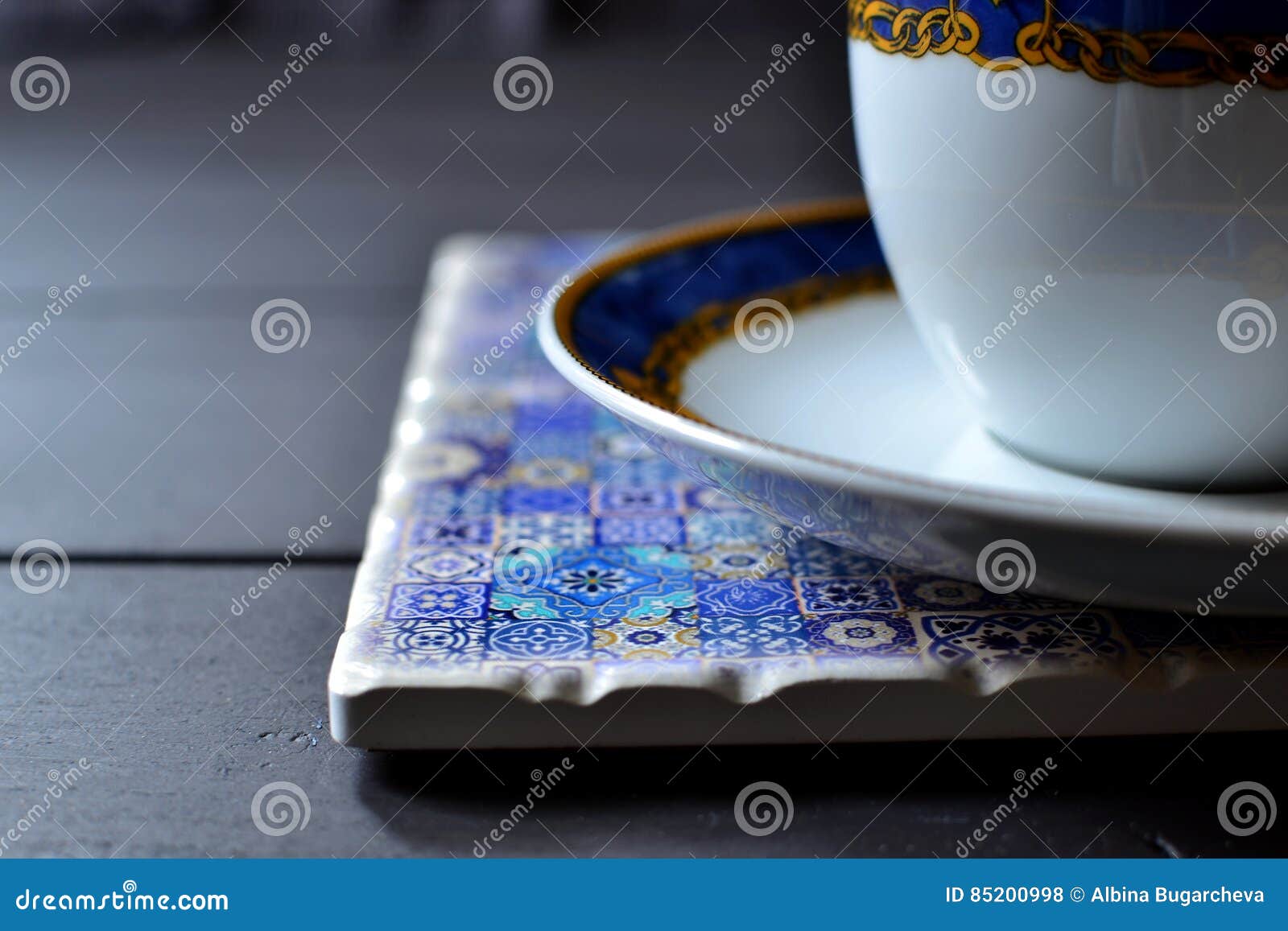 Tea cup and saucer on a placemat. Fine china white tea cup and saucer on a blue colored ornamented ceramic placemat