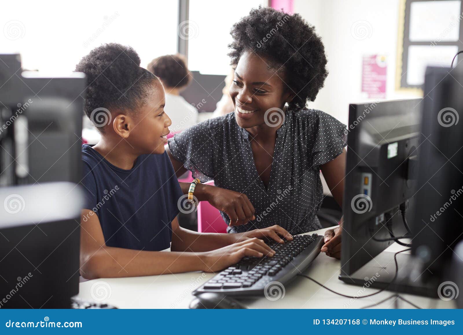teacher helping female high school student working at screen in computer class