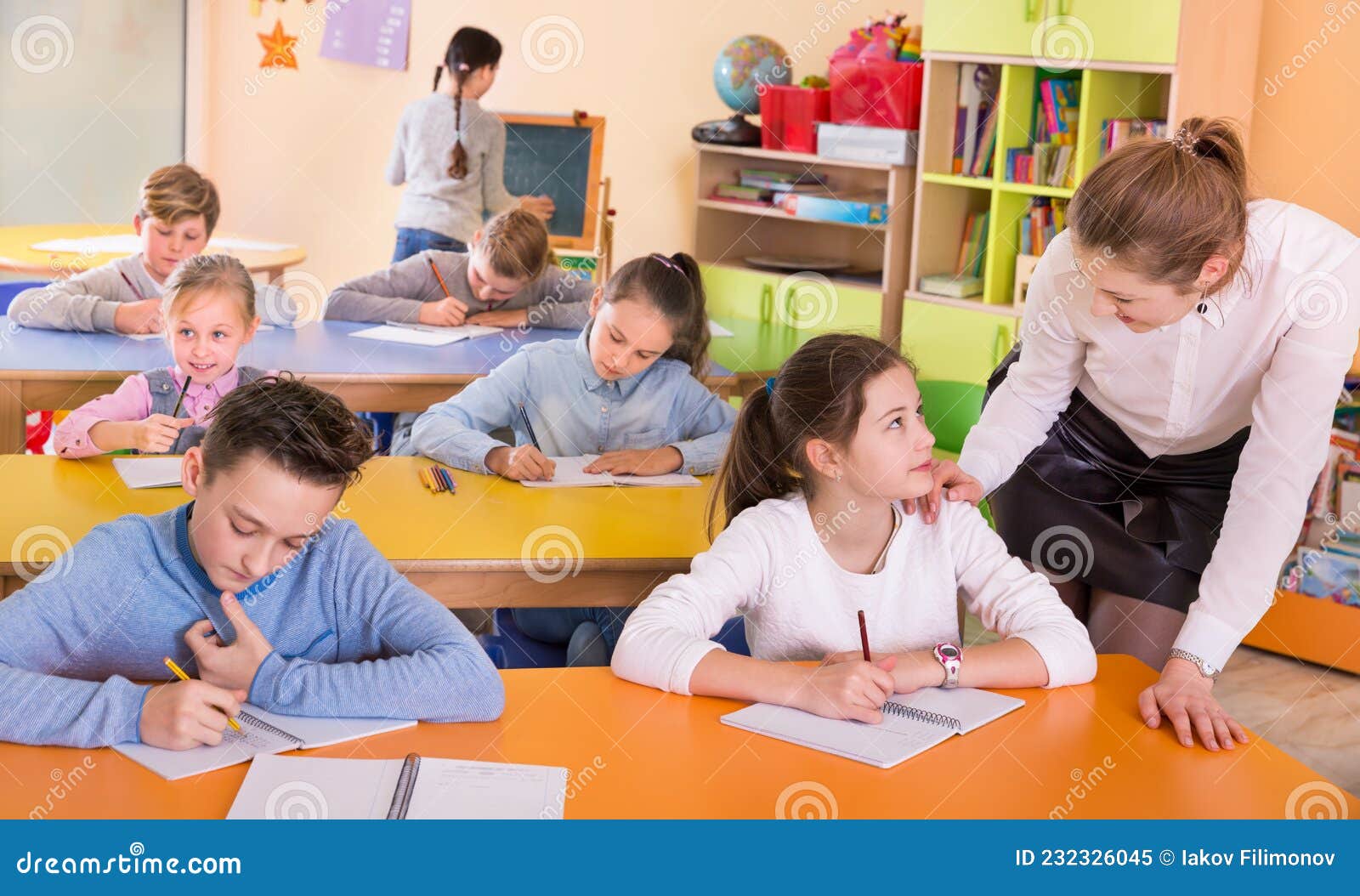 teacher woman helping children during lesson in schoolroom