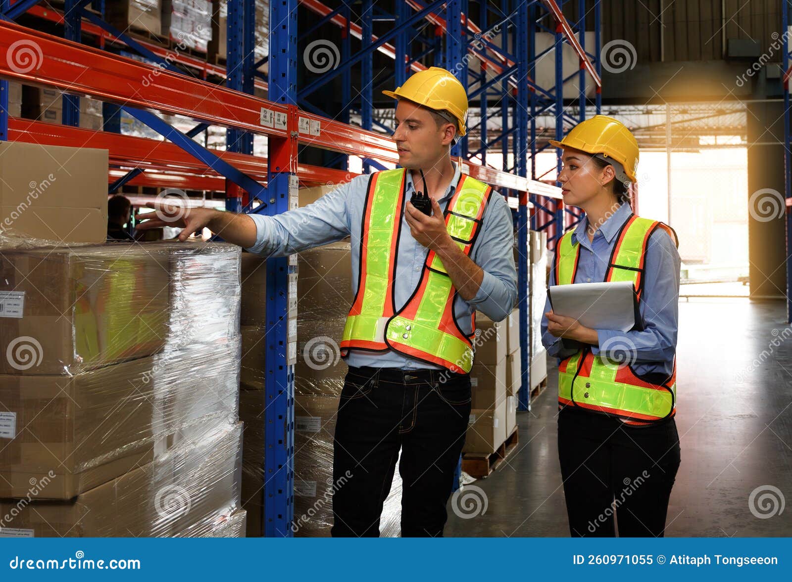 a team of caucasian male and female engineers stood on a shelf stored in a warehouse. use radios and clipboards. check the stock