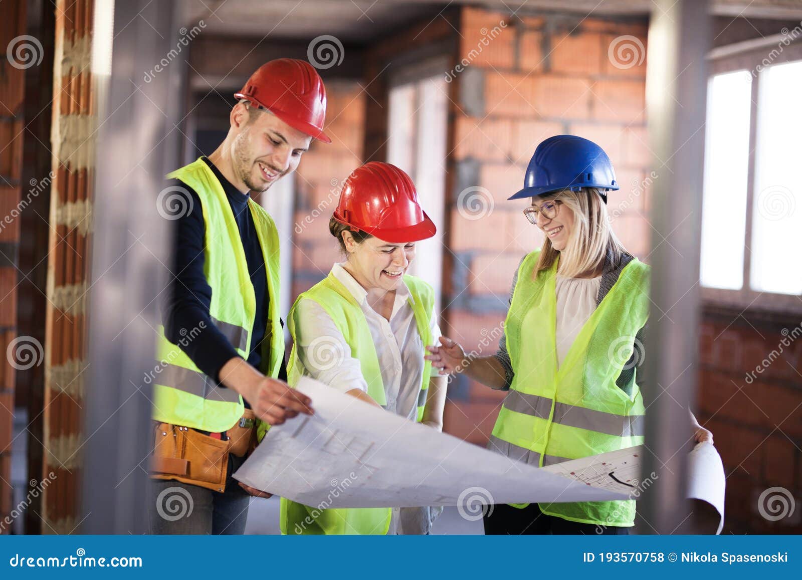Team of Engineers in Vests and Hard Hats with Schematics on a Construction Site Stock Photo